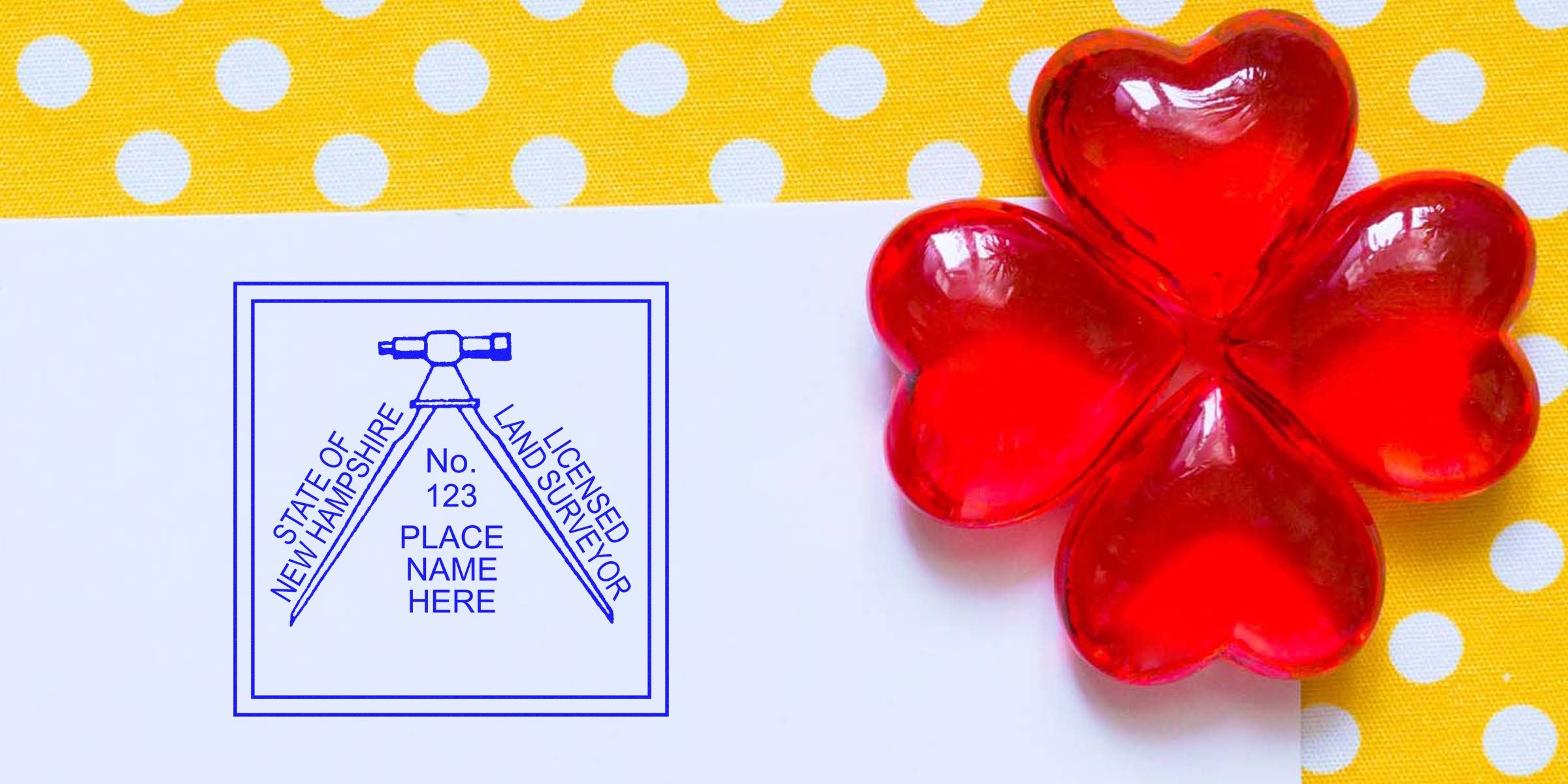 Red heart-shaped candies form a four-leaf clover on a yellow polka dot background next to a New Hampshire land surveyor stamp on white paper, illustrating the land surveyor stamp ordering process.