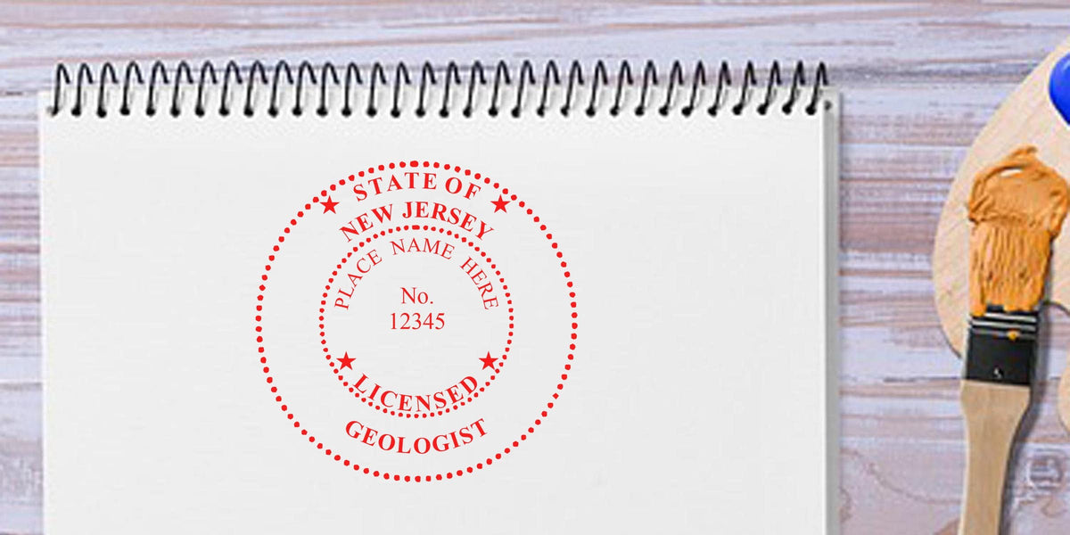 New Jersey Professional Geologist Stamp on white notebook with paintbrush and palette on wooden table, showing Geologist Stamp Requirements NJ.