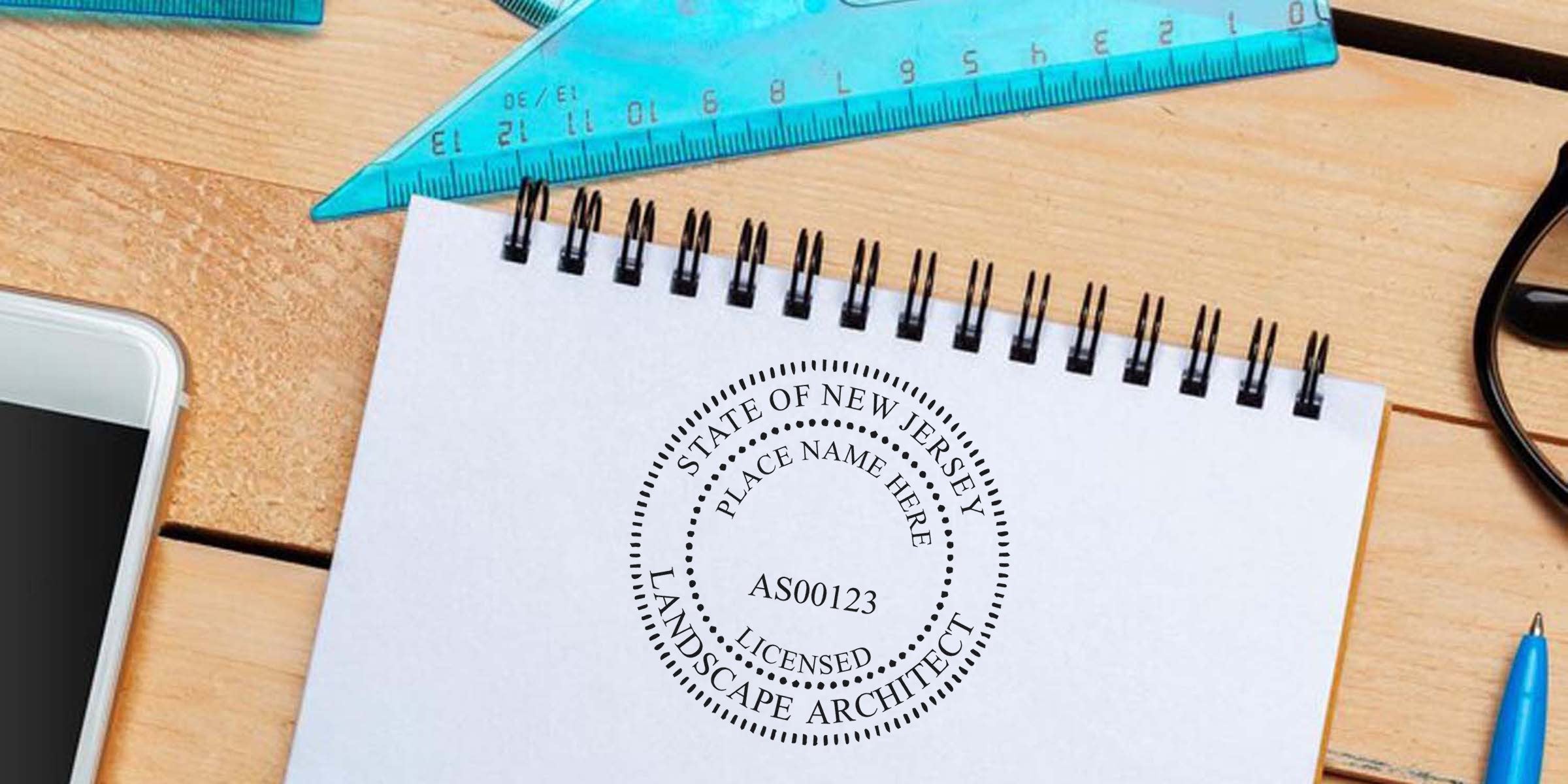 Notepad with New Jersey landscape architect seal, blue ruler, smartphone, and pen on wooden desk, showcasing NJ landscape architect seal requirements.