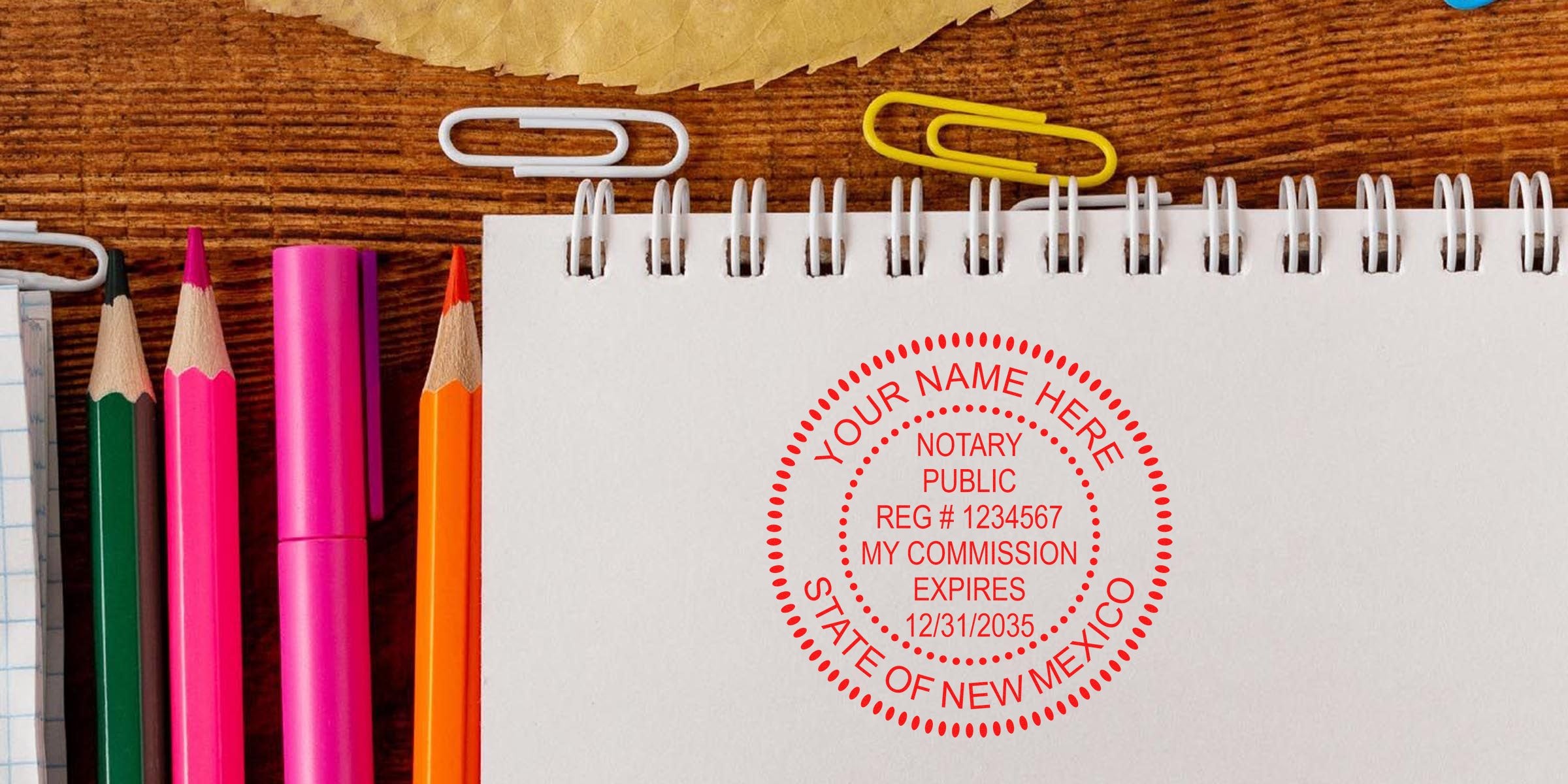 Notary stamp from New Mexico on a white notebook with colored pencils and paper clips on a wooden desk, showcasing trusted notary supplies.