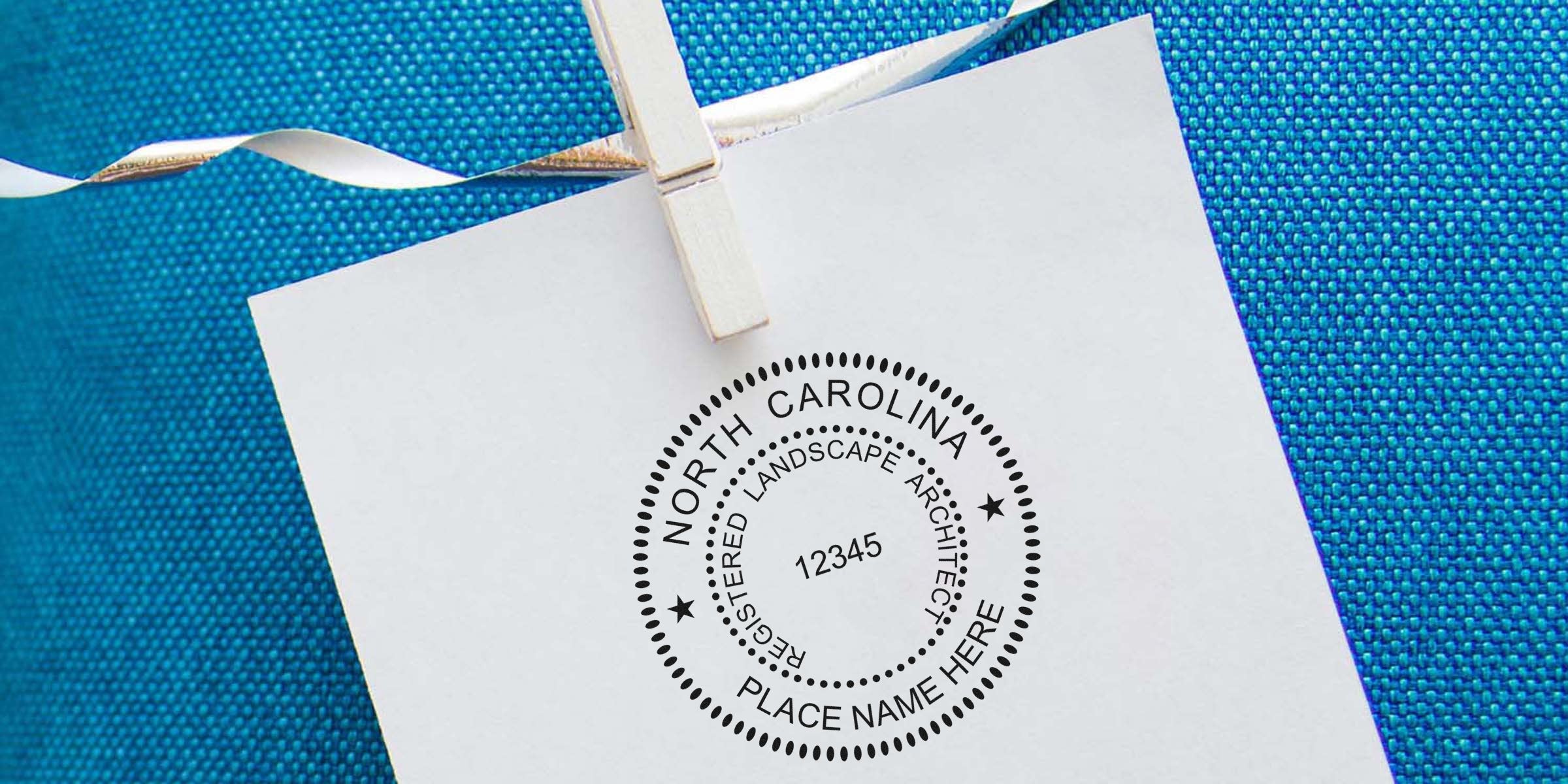 North Carolina landscape architect license stamped on white paper, clipped with a clothespin against blue fabric, meeting NC landscape architect stamp requirements.