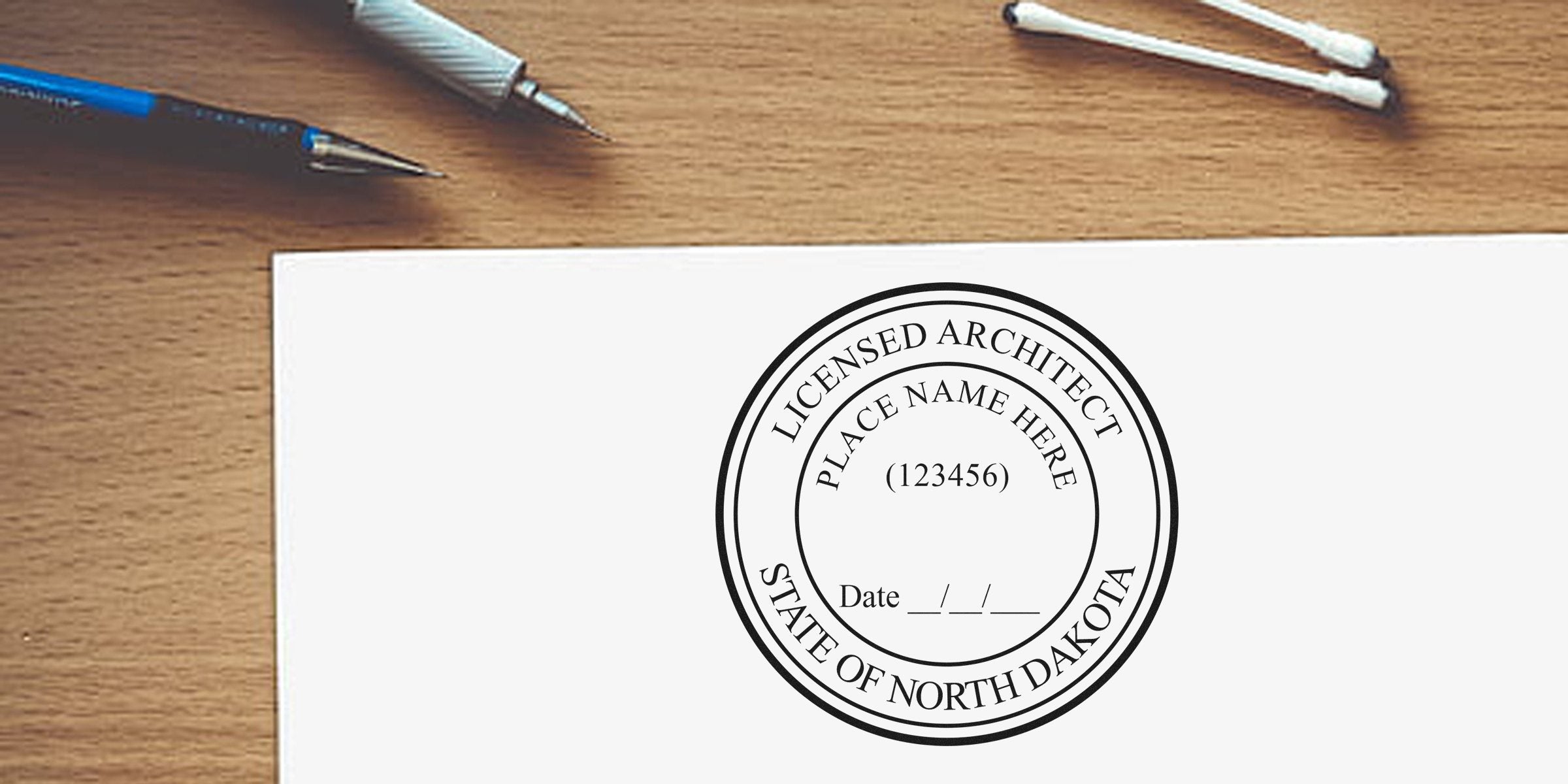 Licensed architect stamp with North Dakota seal on white paper, alongside pens and cotton swabs on a wooden desk, emphasizing architect seal rules.