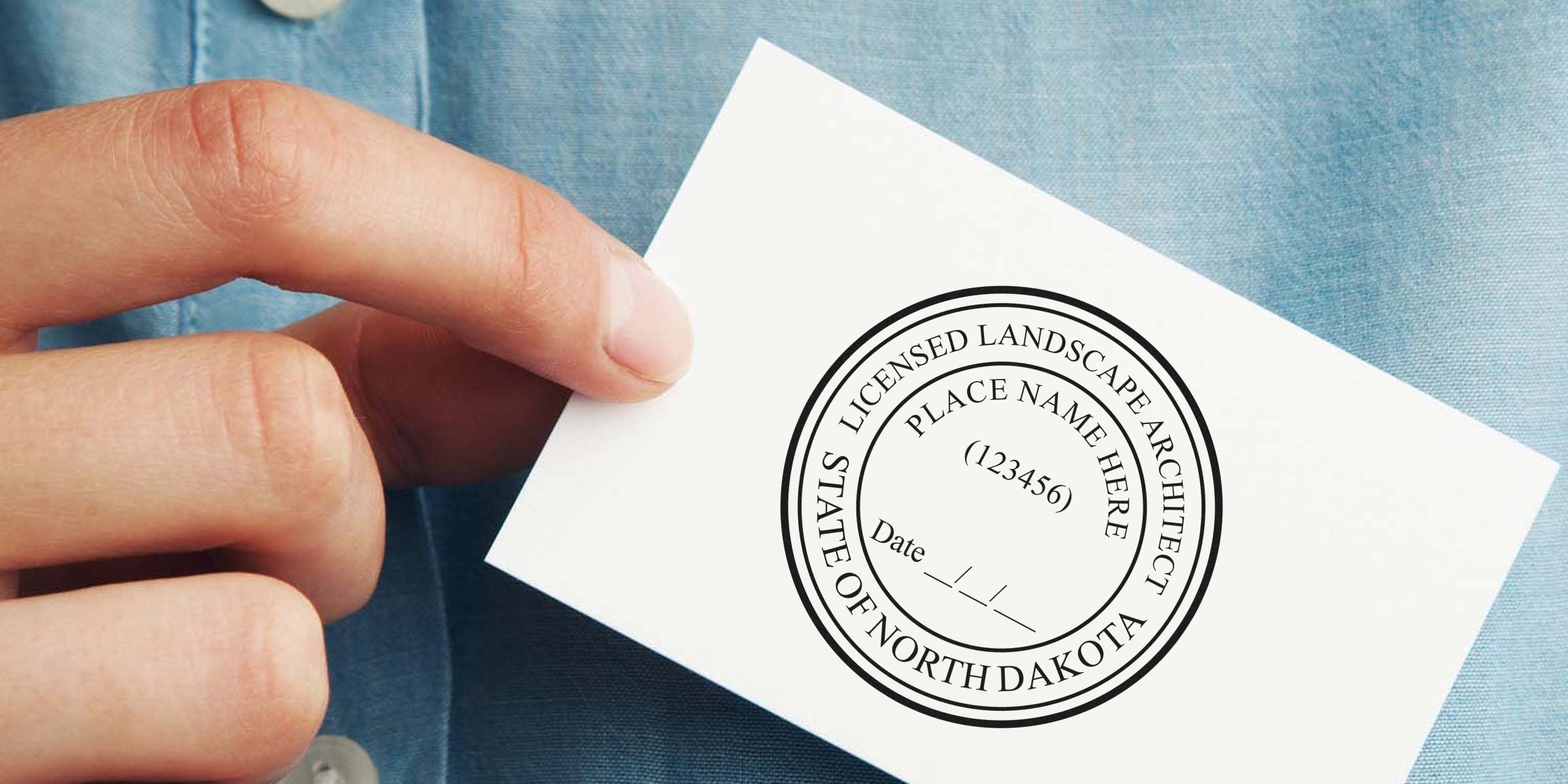 Hand holding a North Dakota landscape architect seal stamp on white paper, showing the official seal design for professional certification.