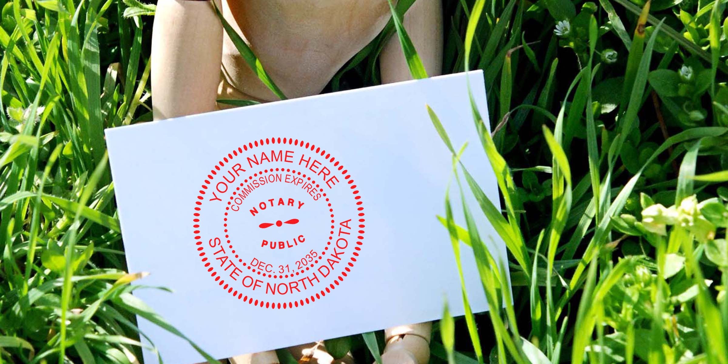 North Dakota notary seal stamped on white paper held in green grass, meeting official legal document requirements.