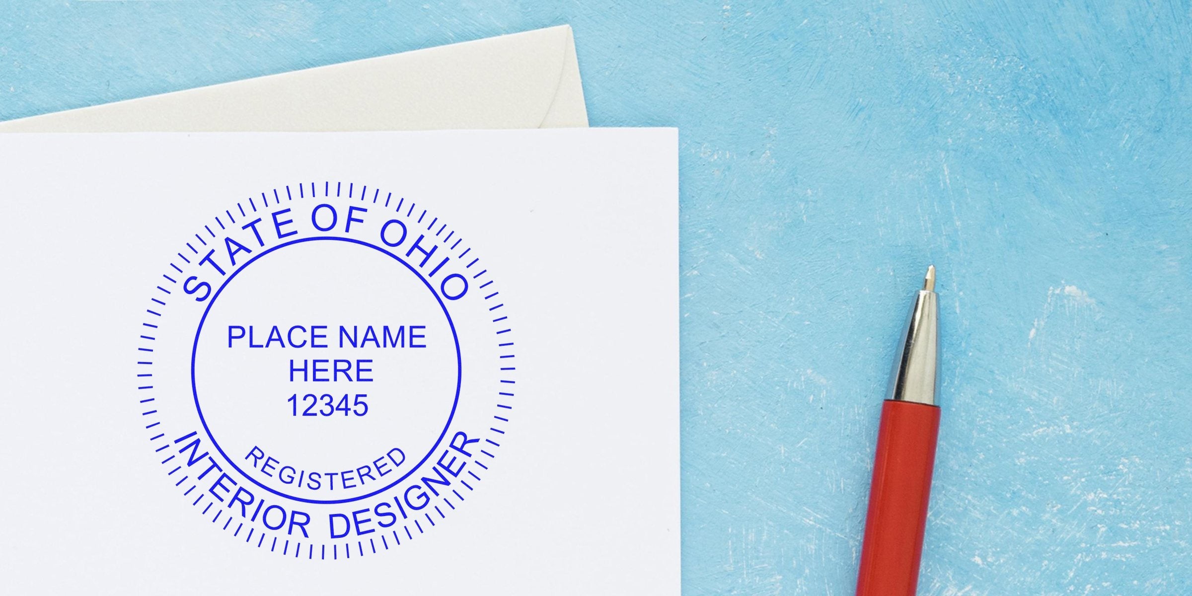 Ohio interior designer seal embosser with registered stamp on white paper, red pen beside it, set against a blue background.