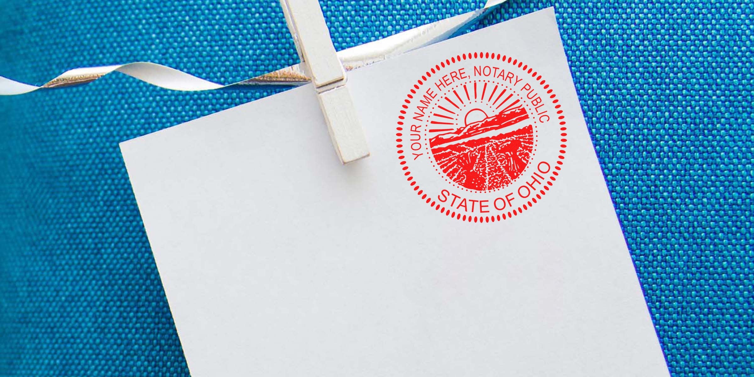 Ohio notary public stamp on white paper clipped with a clothespin against a blue textured background, part of the Ohio notary starter kit for new notaries.