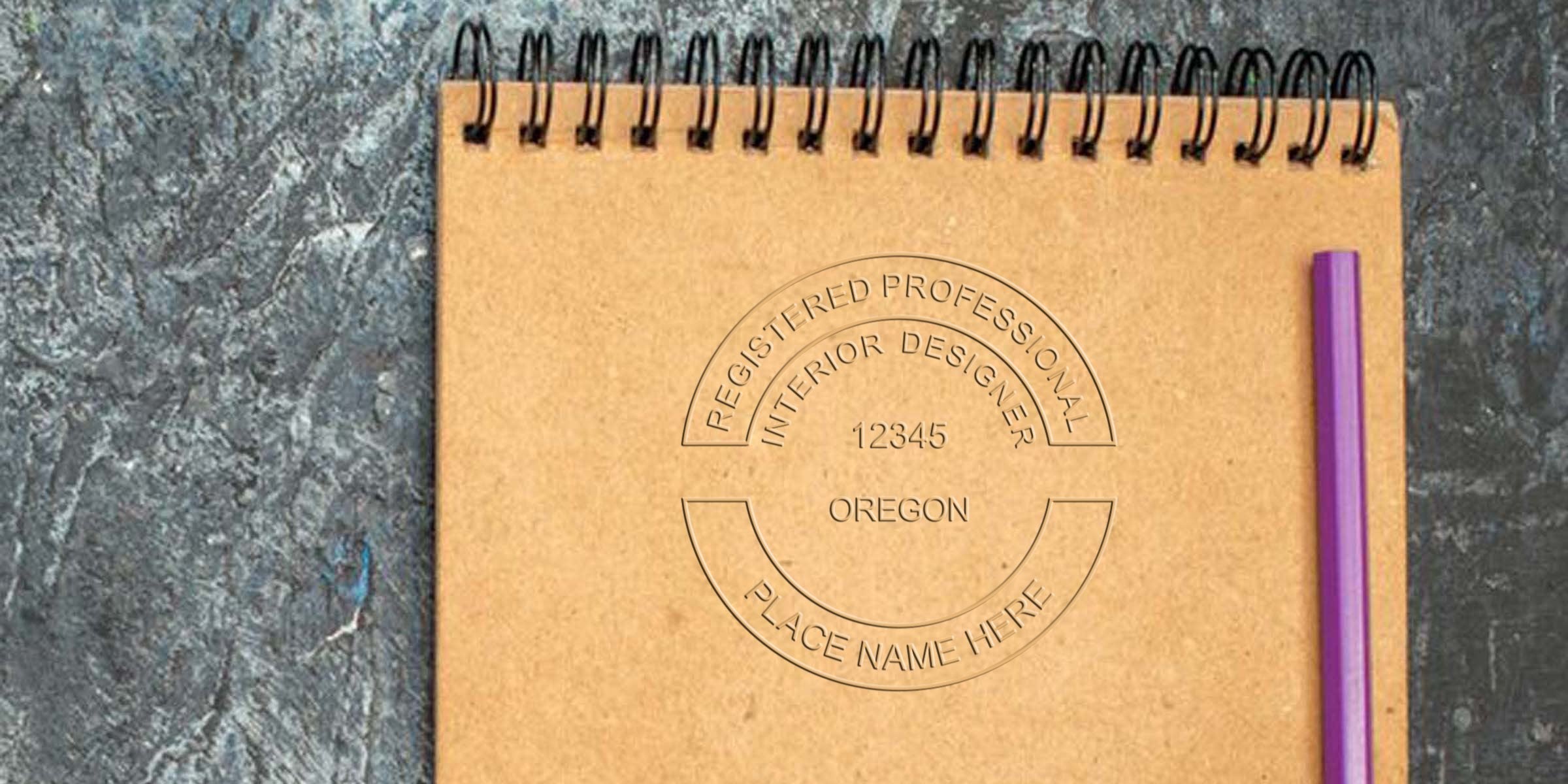 Oregon interior designer stamp on a brown spiral notebook with a purple pen on a textured gray surface, showing registered professional interior designer certification and stamp requirements in Oregon.