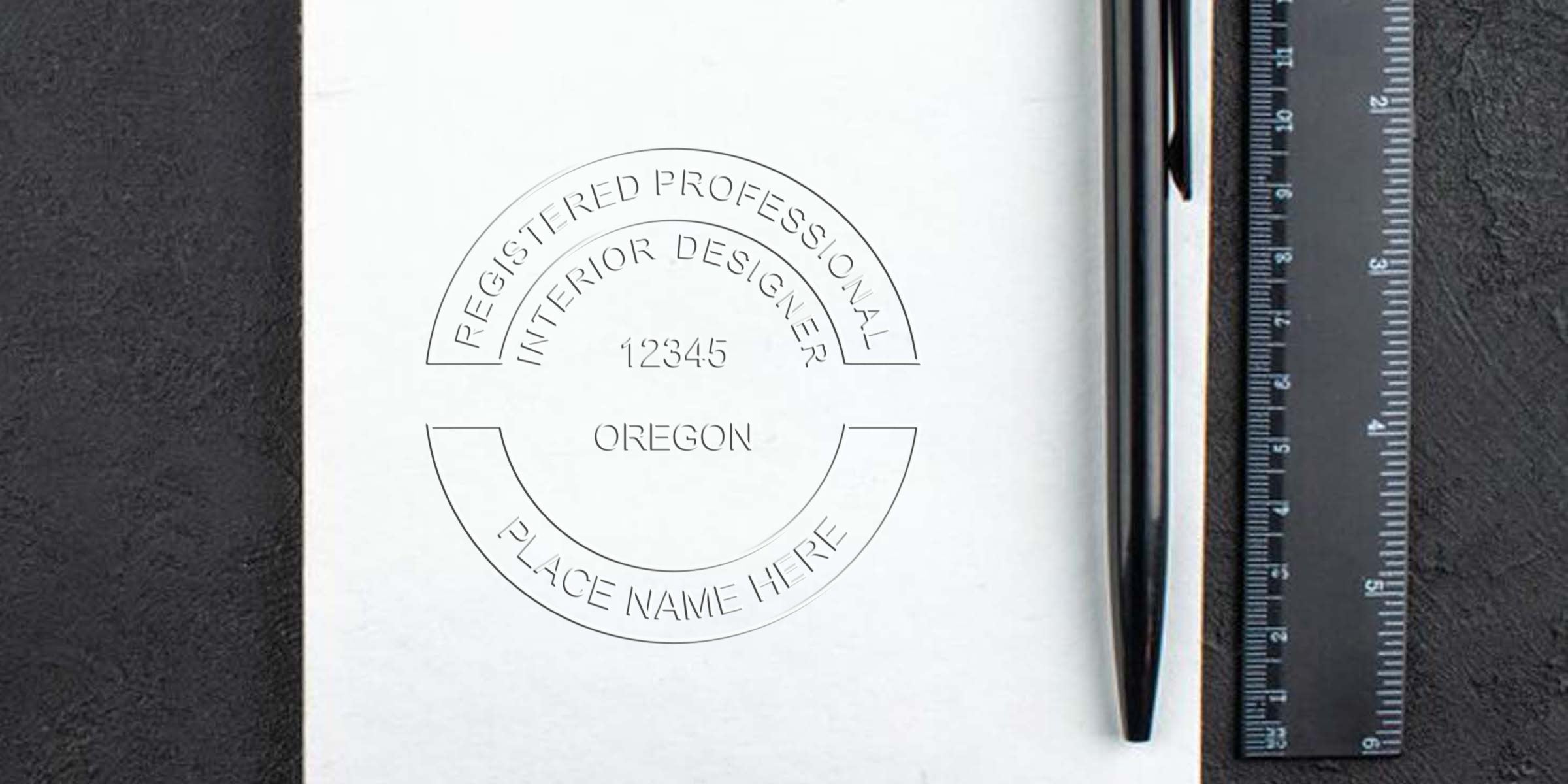 Oregon designer stamps with a registered interior designer seal on paper, alongside a black pen and ruler, used for certification and license verification with custom rubber stamps.