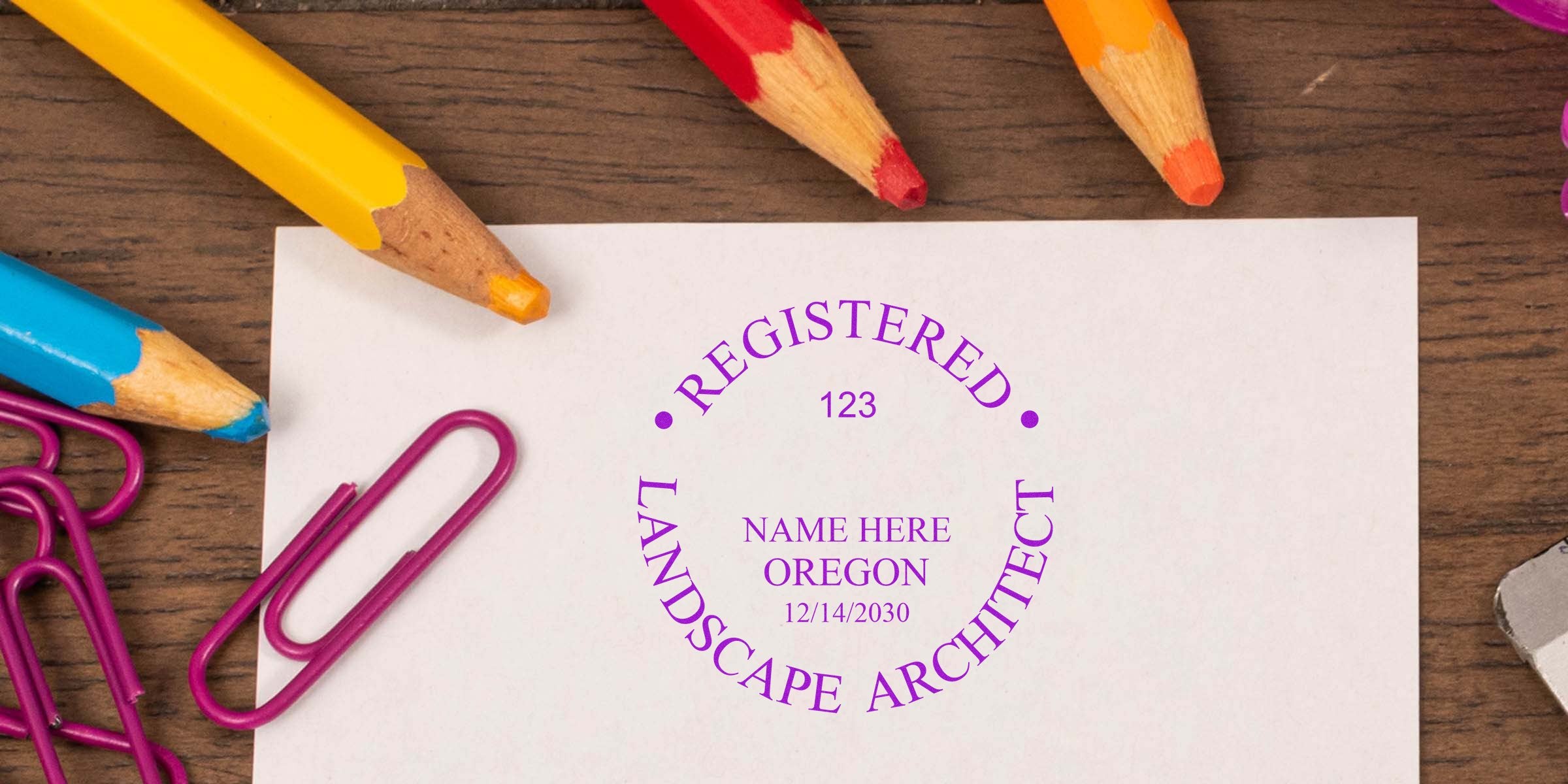 Registered Landscape Architect stamp in Oregon with colorful pencils and paper clips on a wooden desk, emphasizing Oregon Landscape Architect costs.