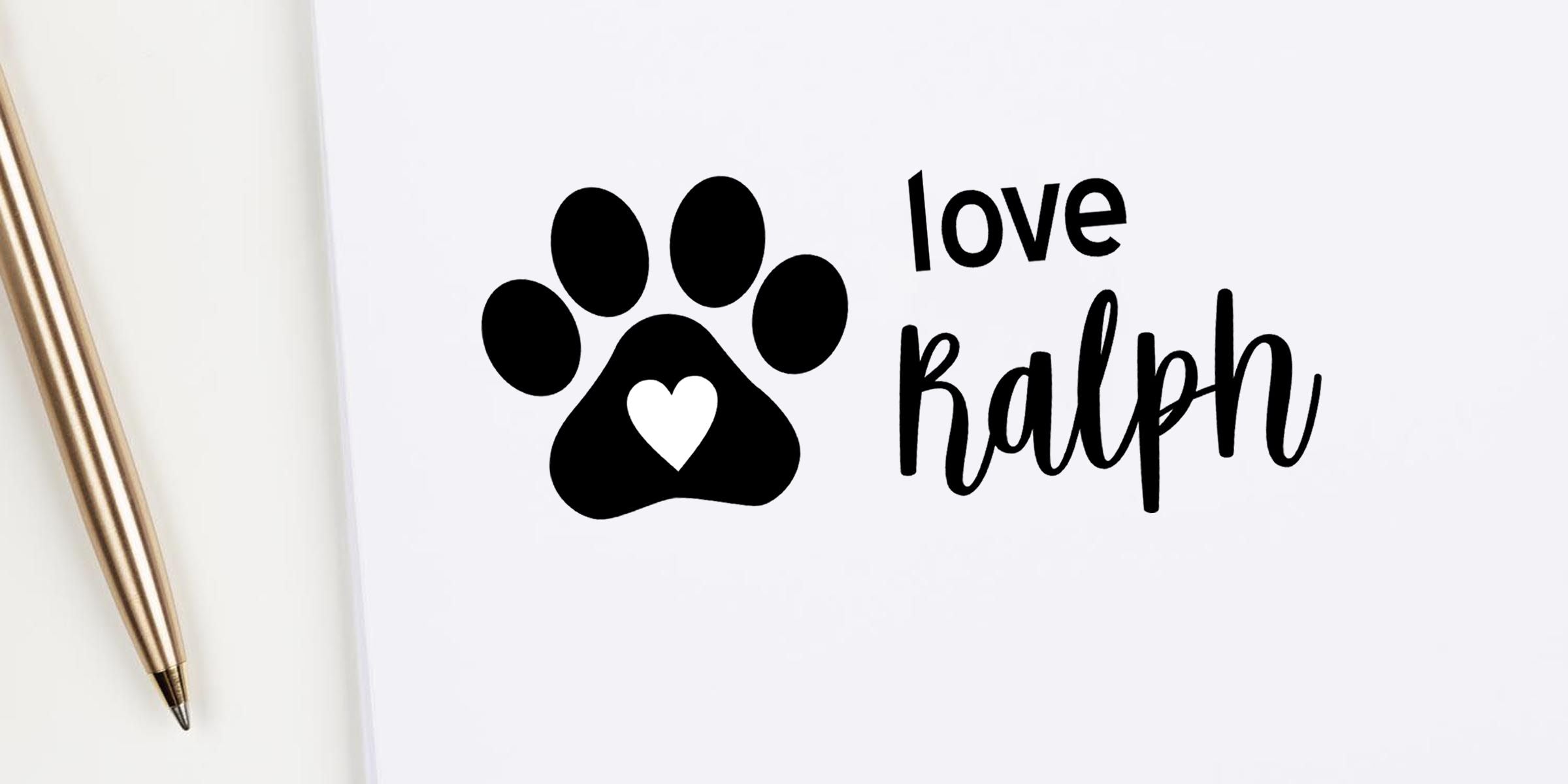 Black paw print with heart and the words love Ralph on a white background beside a gold pen