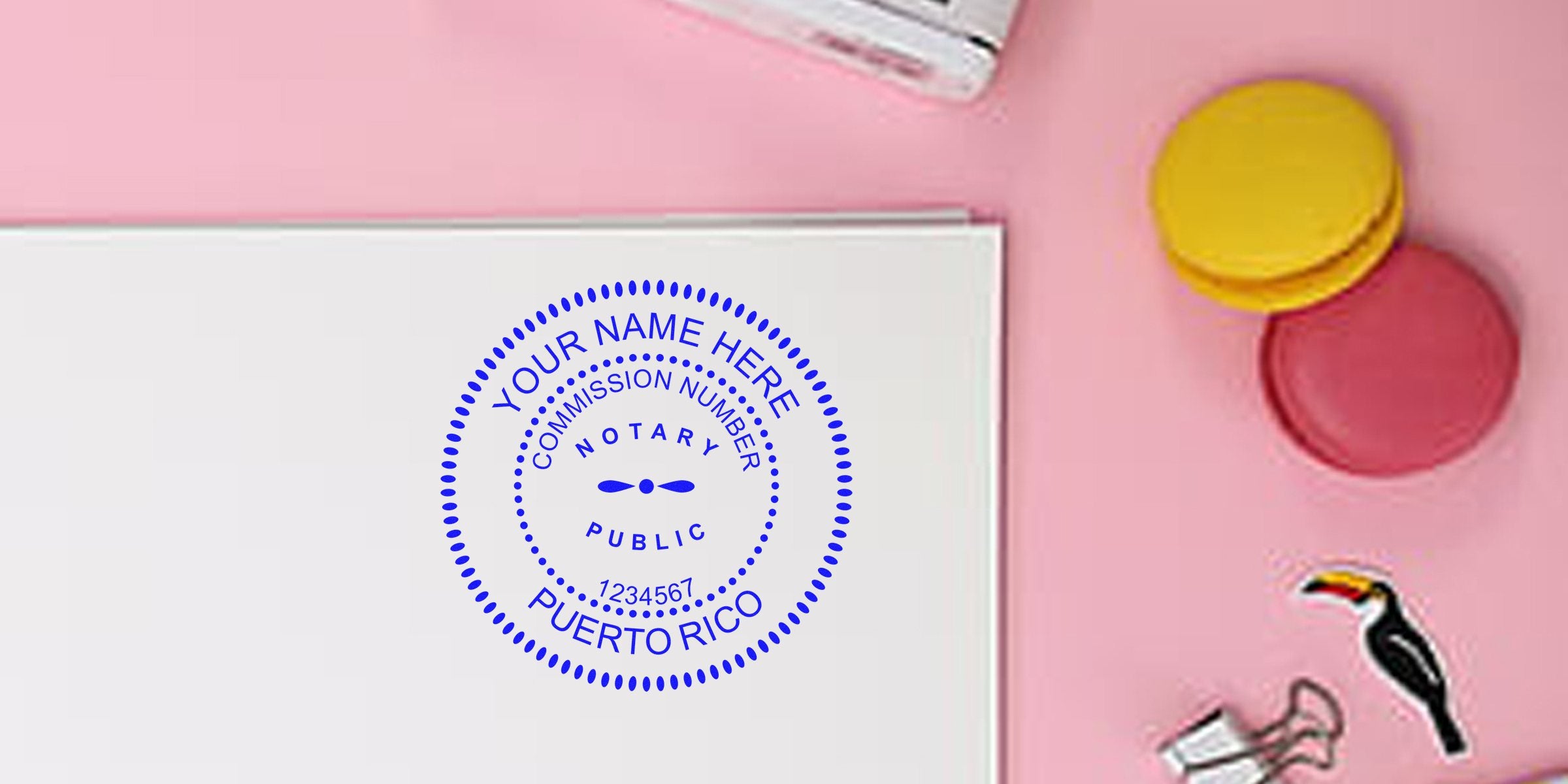 PR notary stamp with commission number on white paper, surrounded by colorful macarons and office supplies on a pink background, shown in a notary stamp buying guide.