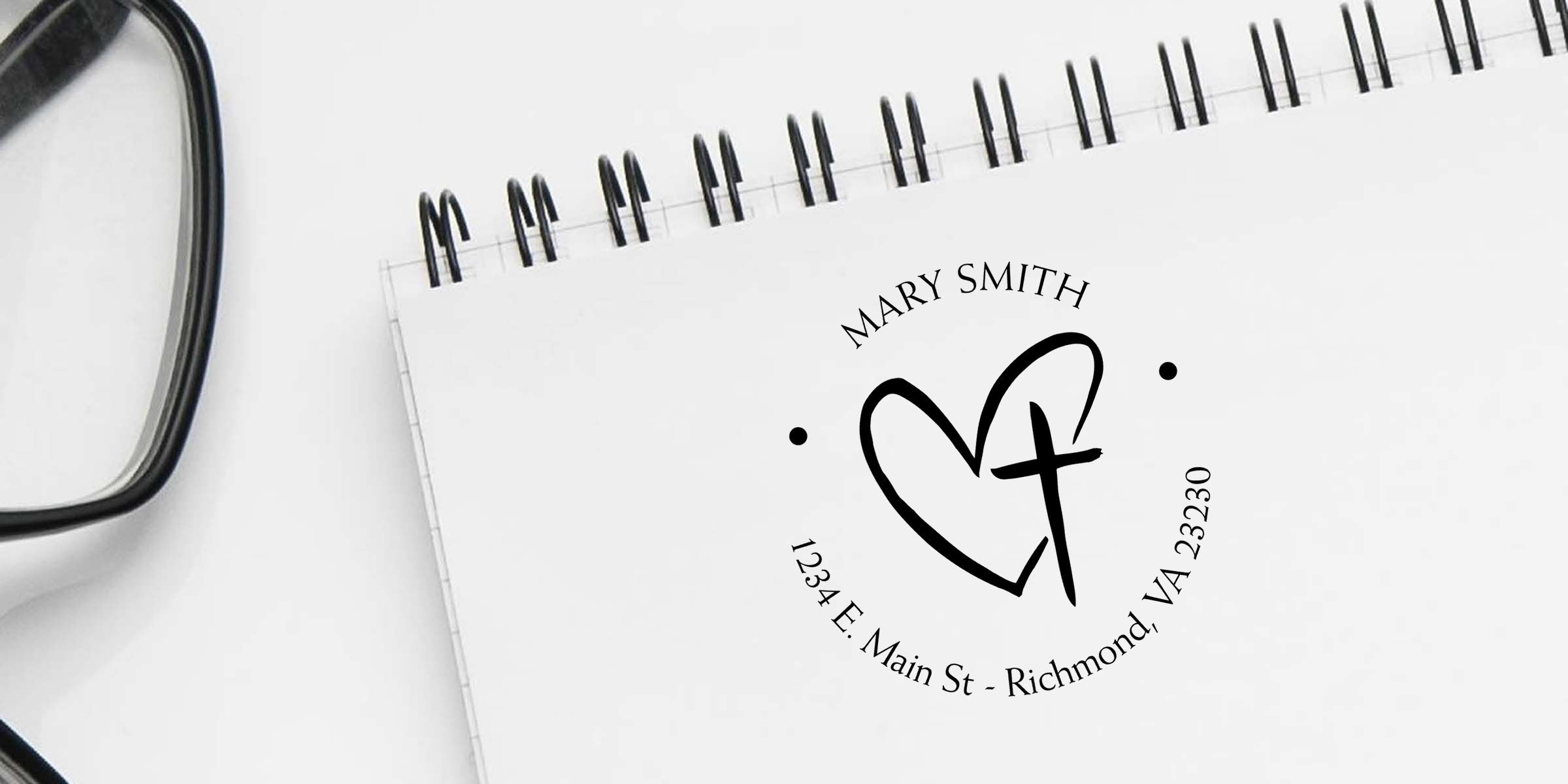 Personalized spiral notebook with heart and cross logo, Mary Smith name, and Richmond, VA address beside eyeglasses