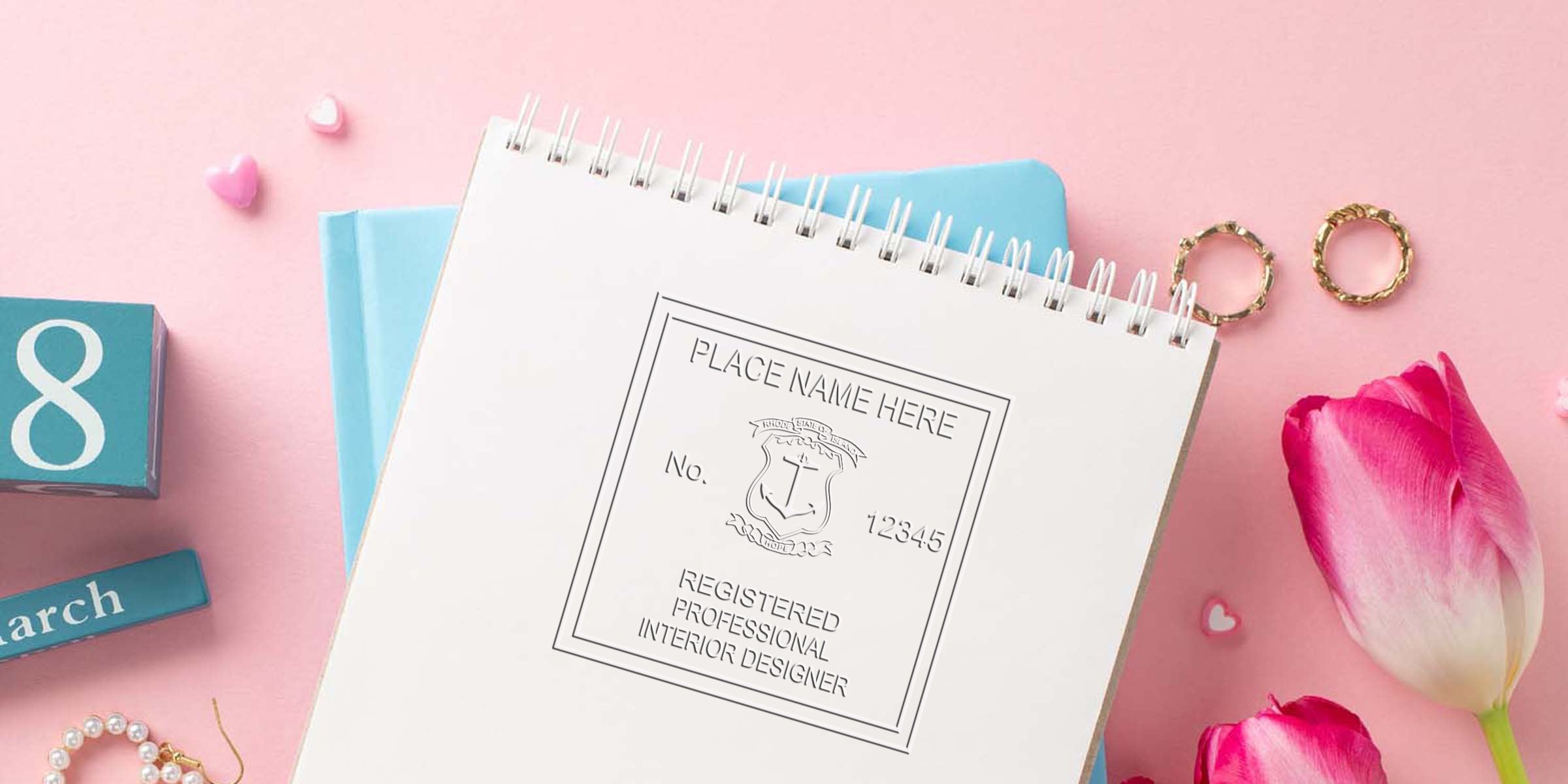 Registered interior designer certificate with Rhode Island stamp on a spiral notebook, surrounded by pink tulips and gold rings on a pastel pink background, highlighting Rhode Island interior design stamp requirements.
