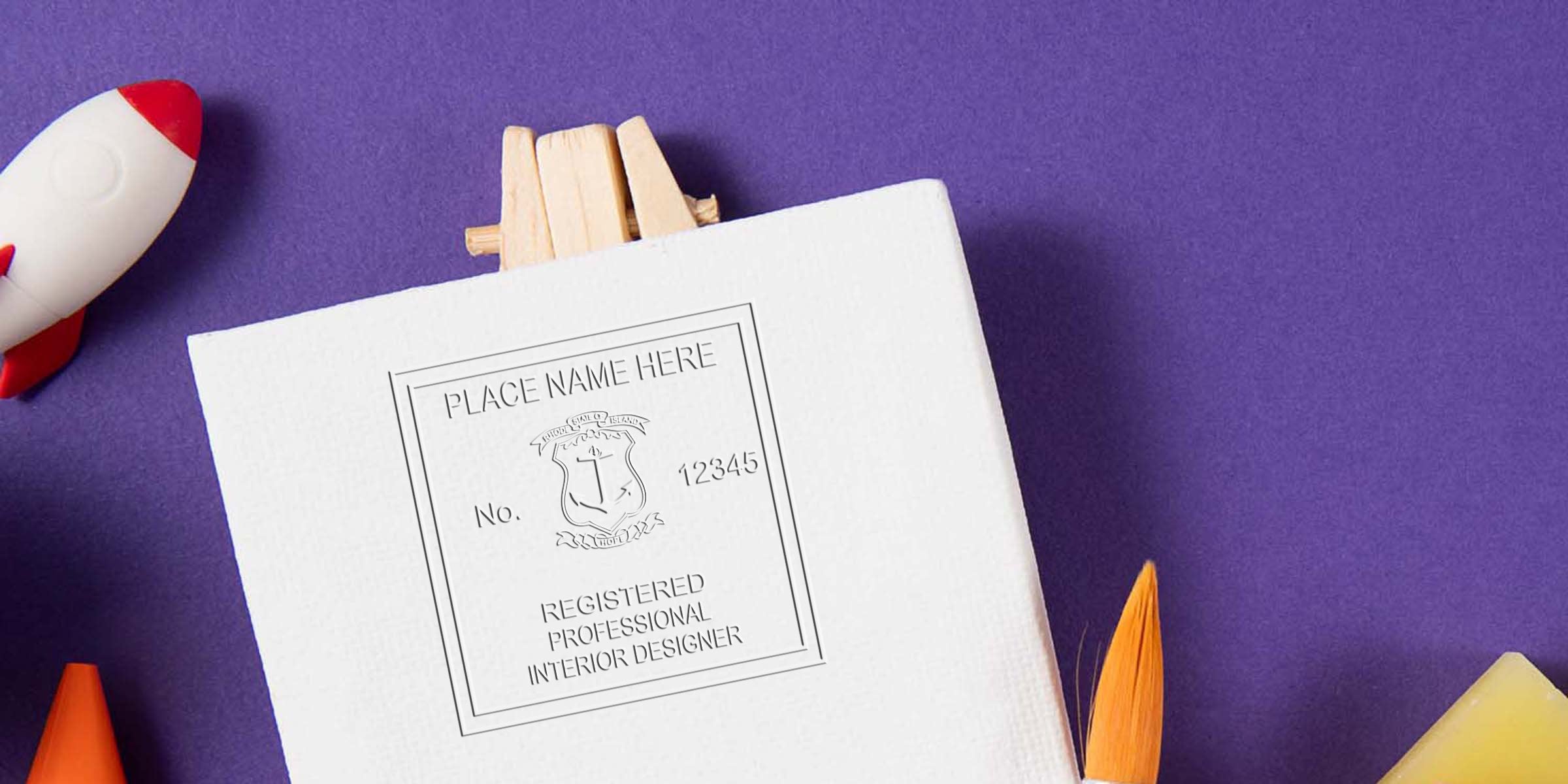 White canvas with Rhode Island interior designer seal, paintbrush, and toy rocket on purple background symbolizing interior design certification and creative art tools.