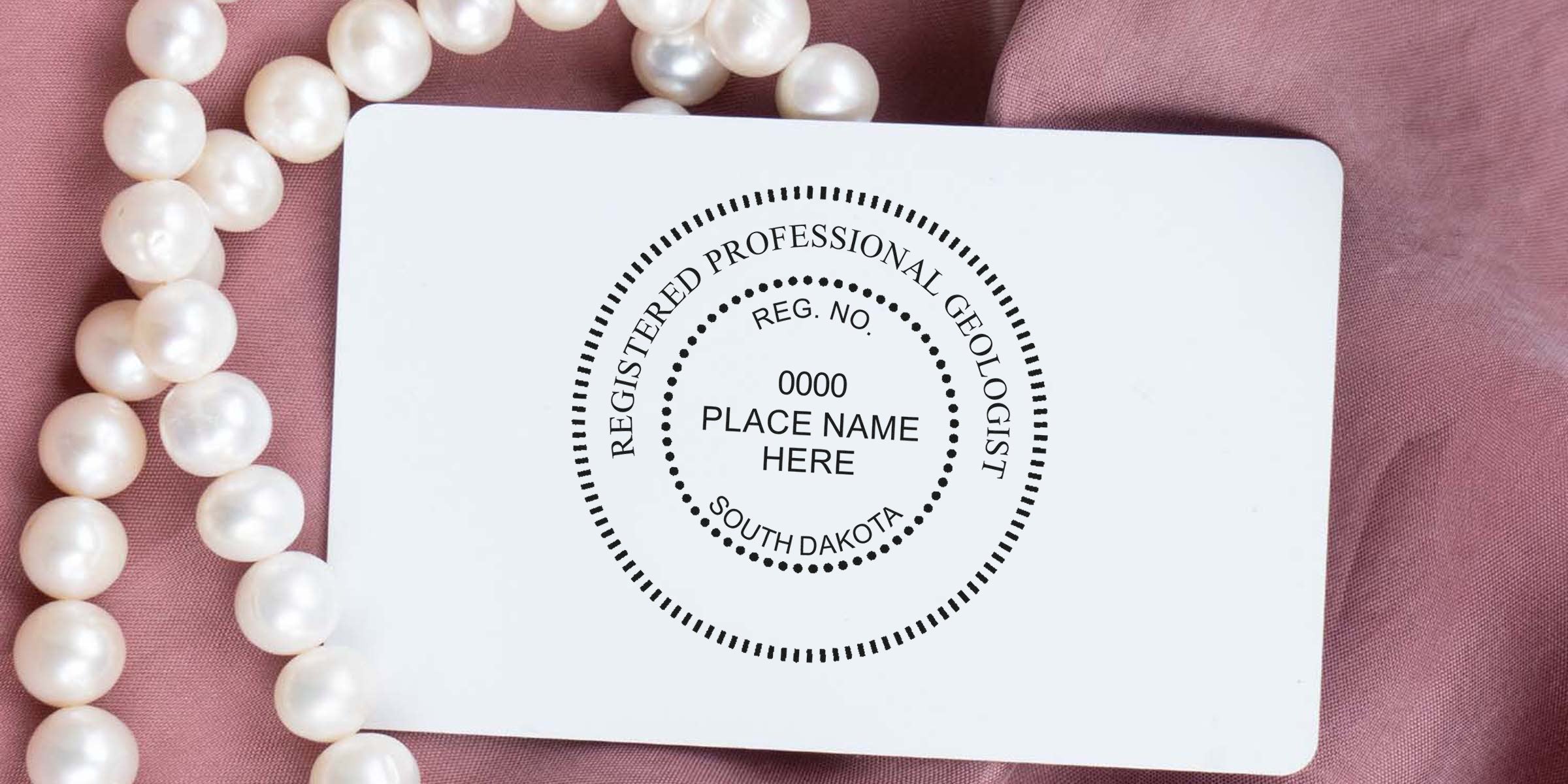 South Dakota geologist stamp on white card with pearl necklace on pink fabric, showing South Dakota registered professional geologist seal and following geologist stamp guidelines.