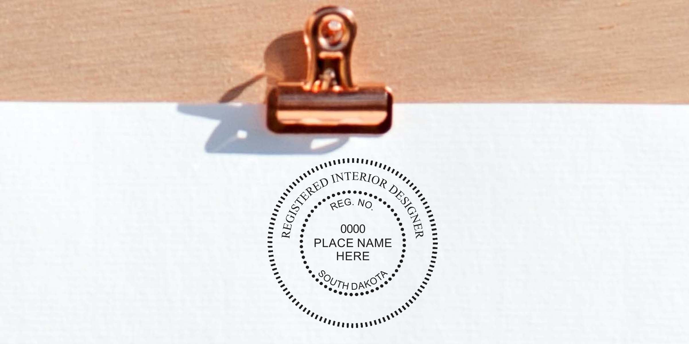 Registered interior designer stamp on white paper with copper clip, featuring South Dakota official interior design seal per certification guidelines.