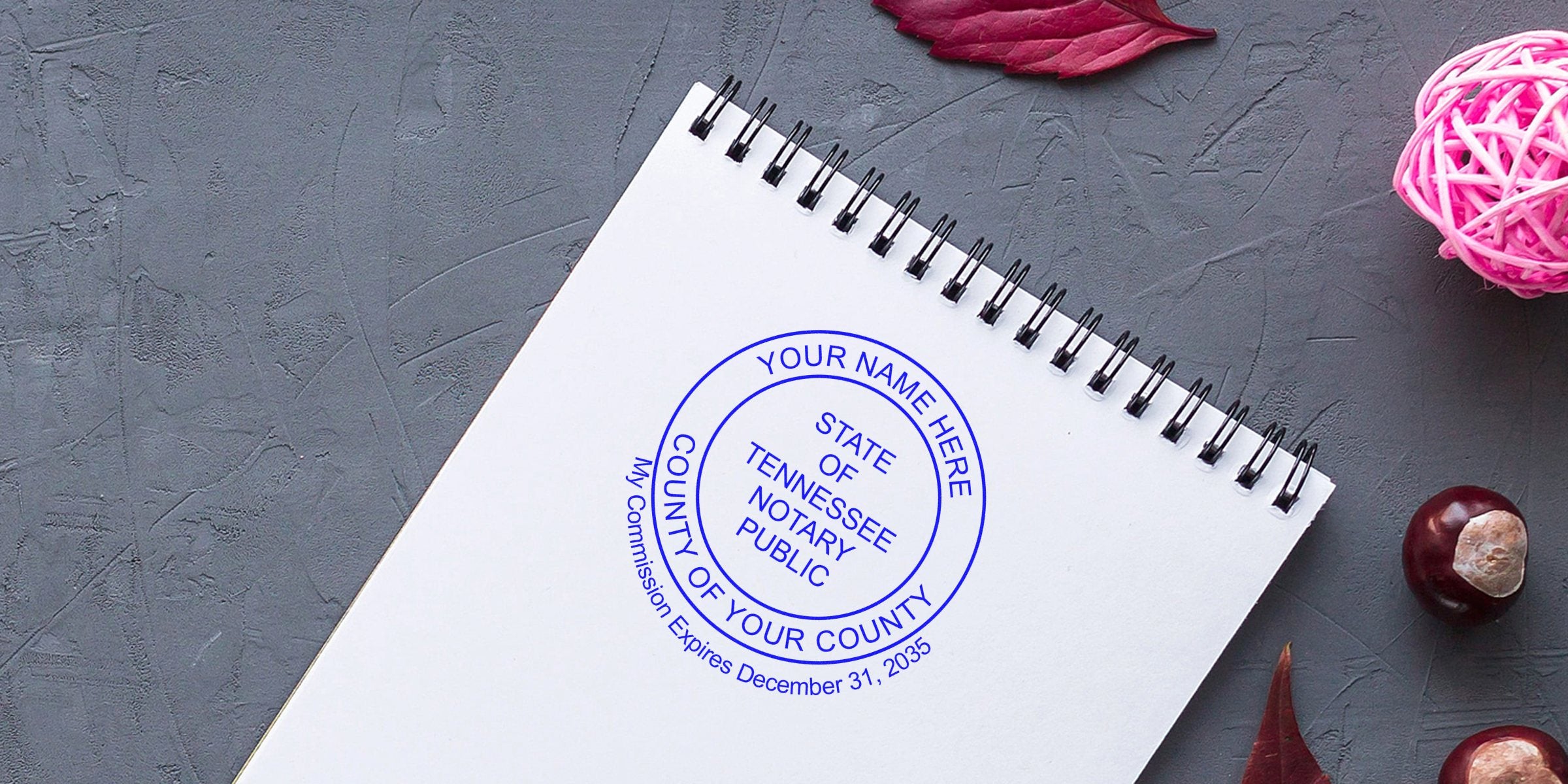 Tennessee notary stamp on white spiral notebook with autumn leaves and chestnuts on gray background, illustrating Tennessee notary stamp law and requirements.