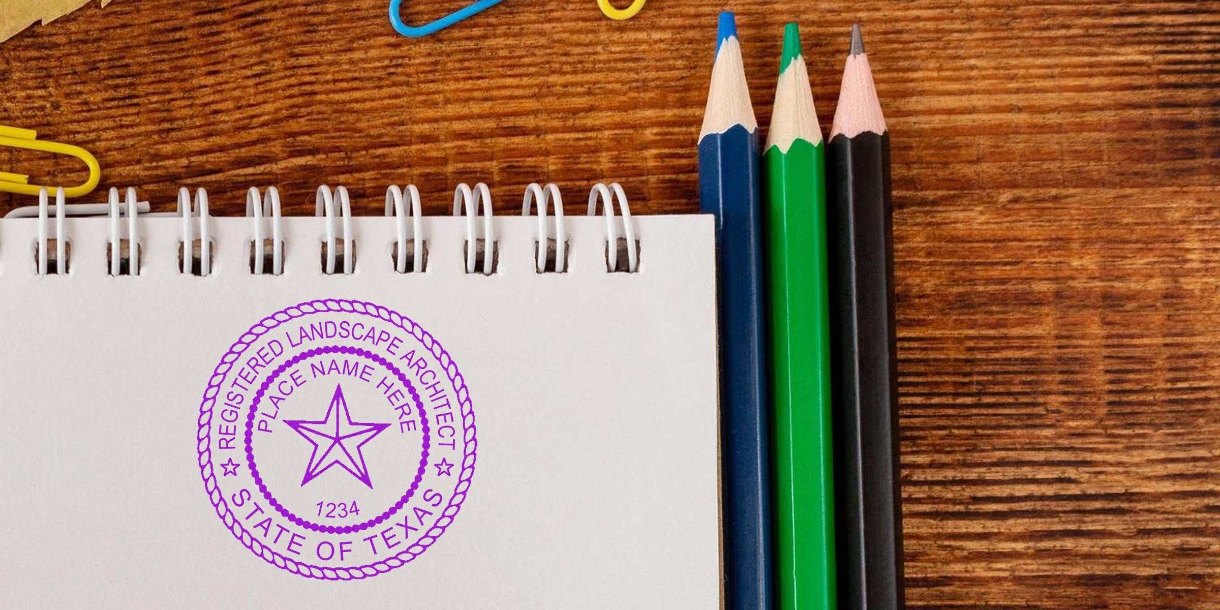 Texas Landscape Architect stamp on notebook with colored pencils and paper clips on wooden desk, related to Texas Landscape Architect application.