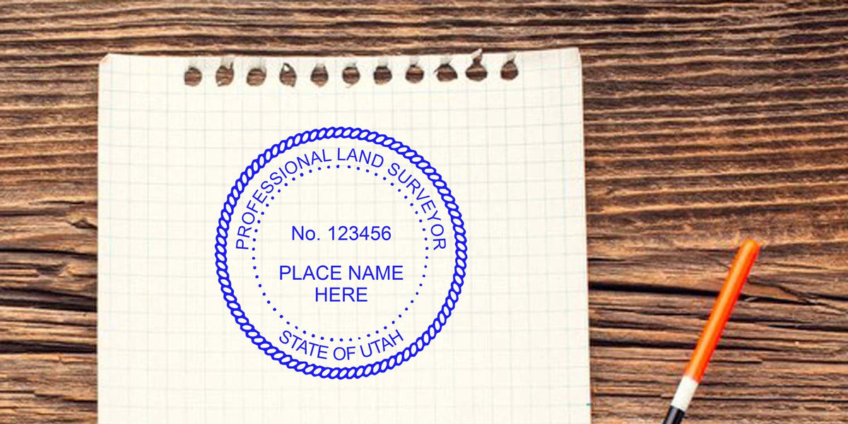 Professional land surveyor stamp with Utah seal on graph paper, orange pen, embosser tips, and surveying tools on a wooden table.