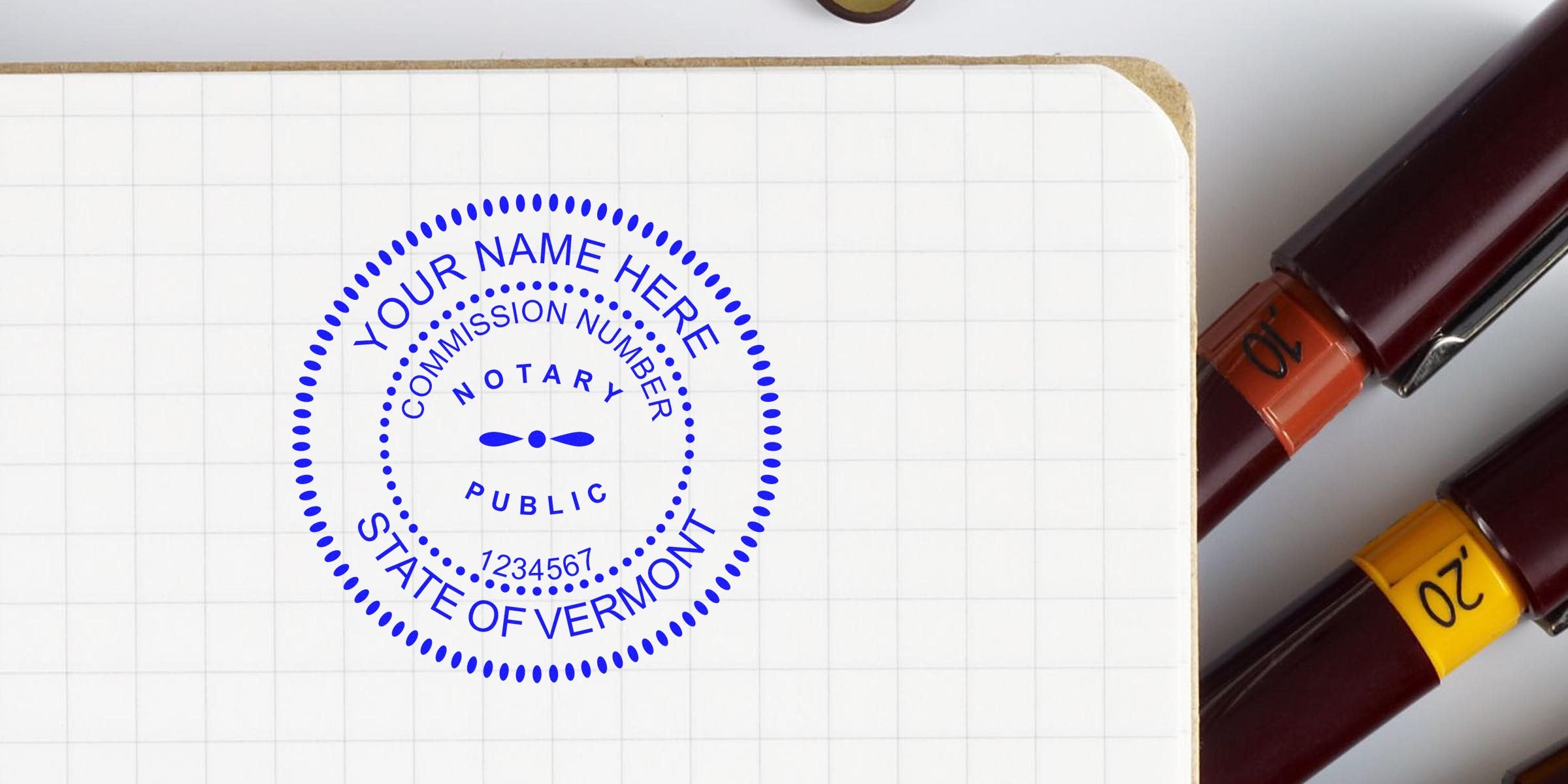 Vermont notary stamp on grid notebook page with two fountain pens nearby, showing business notary essentials.