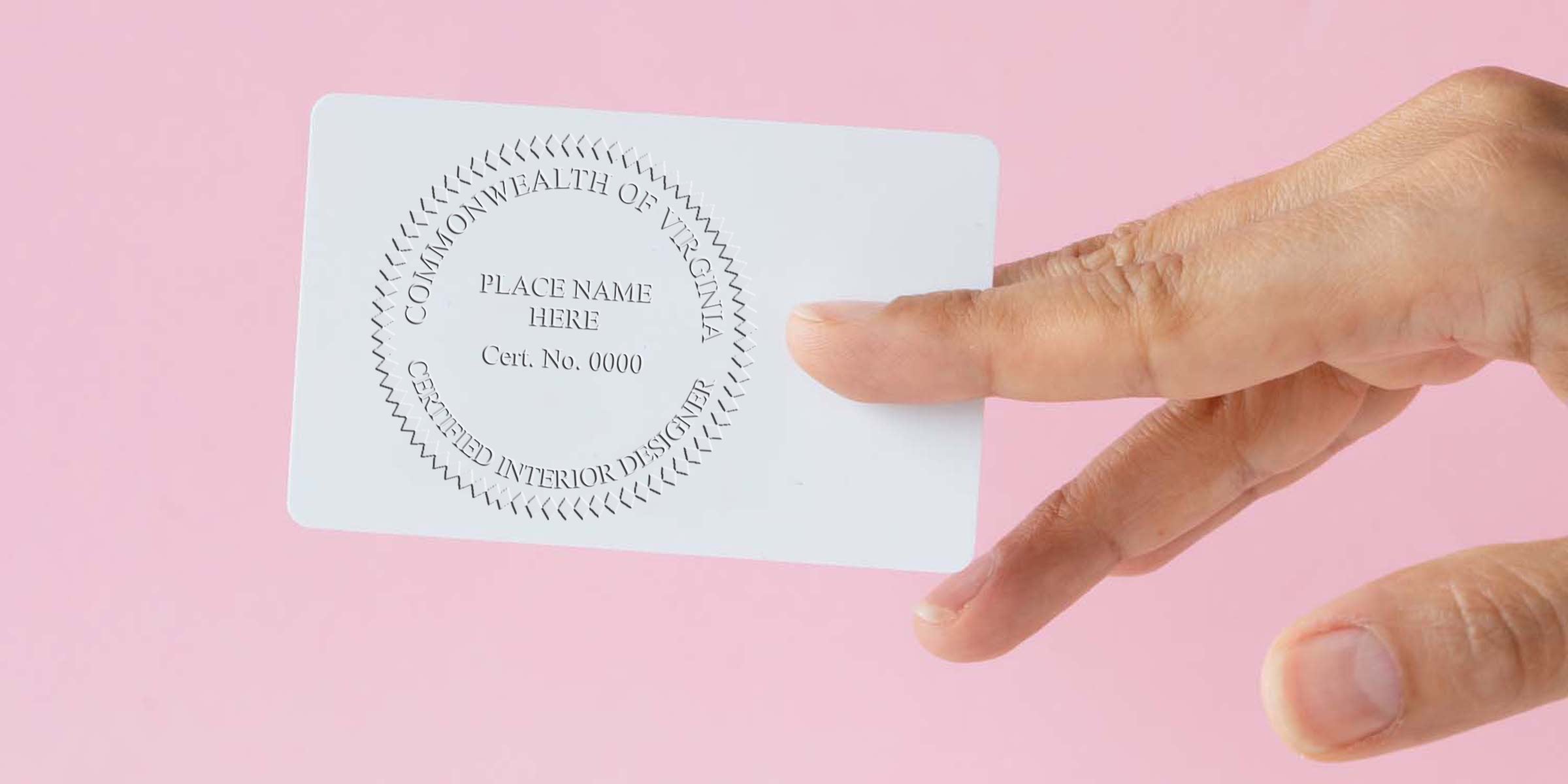 Hand holding Virginia interior designer license card with licensing stamp on pink background.