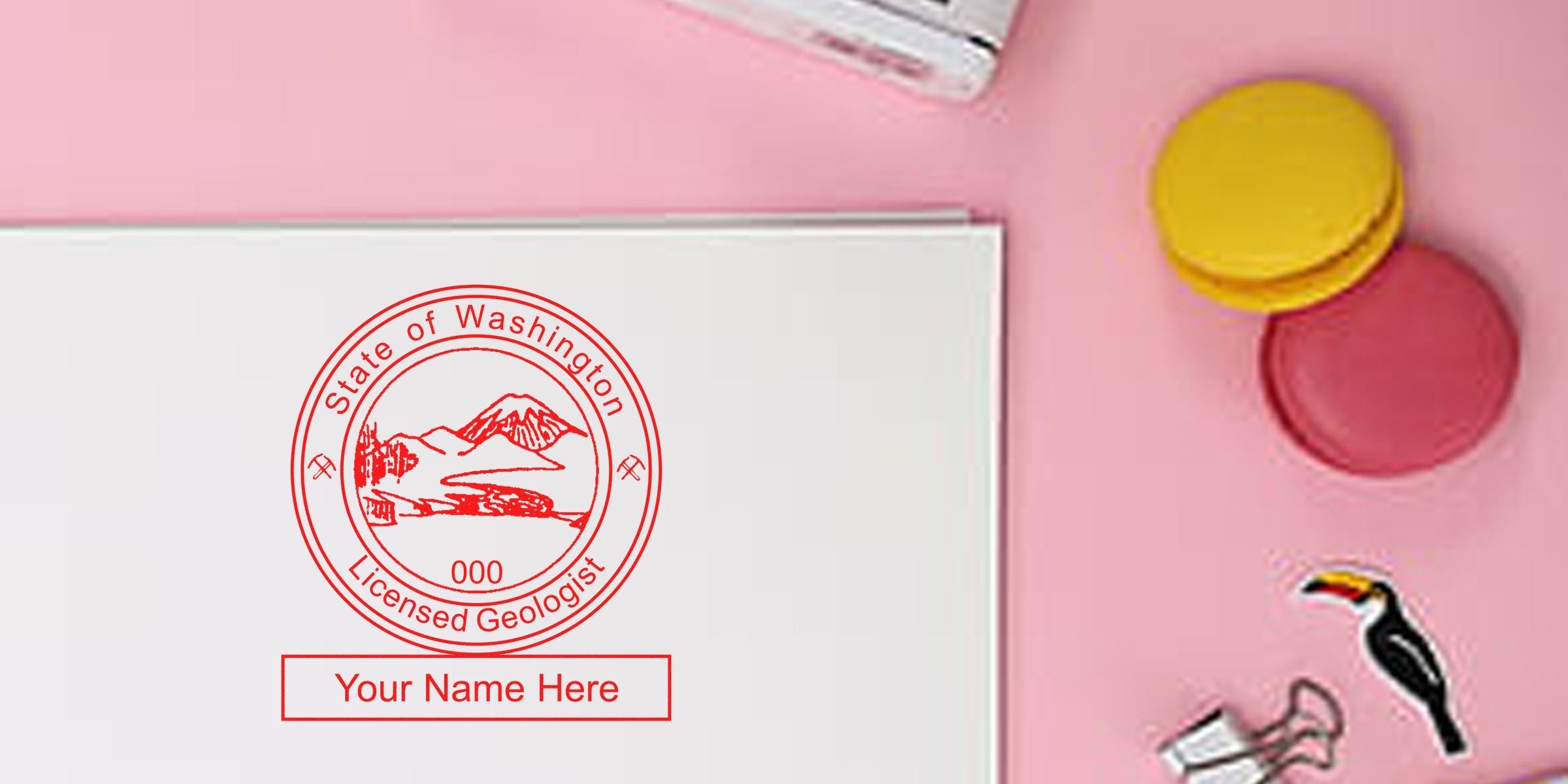 Red-inked Washington geologist seal on white paper with customizable name, colorful macarons on pink background, showcasing the benefits of the geologist seal embosser.
