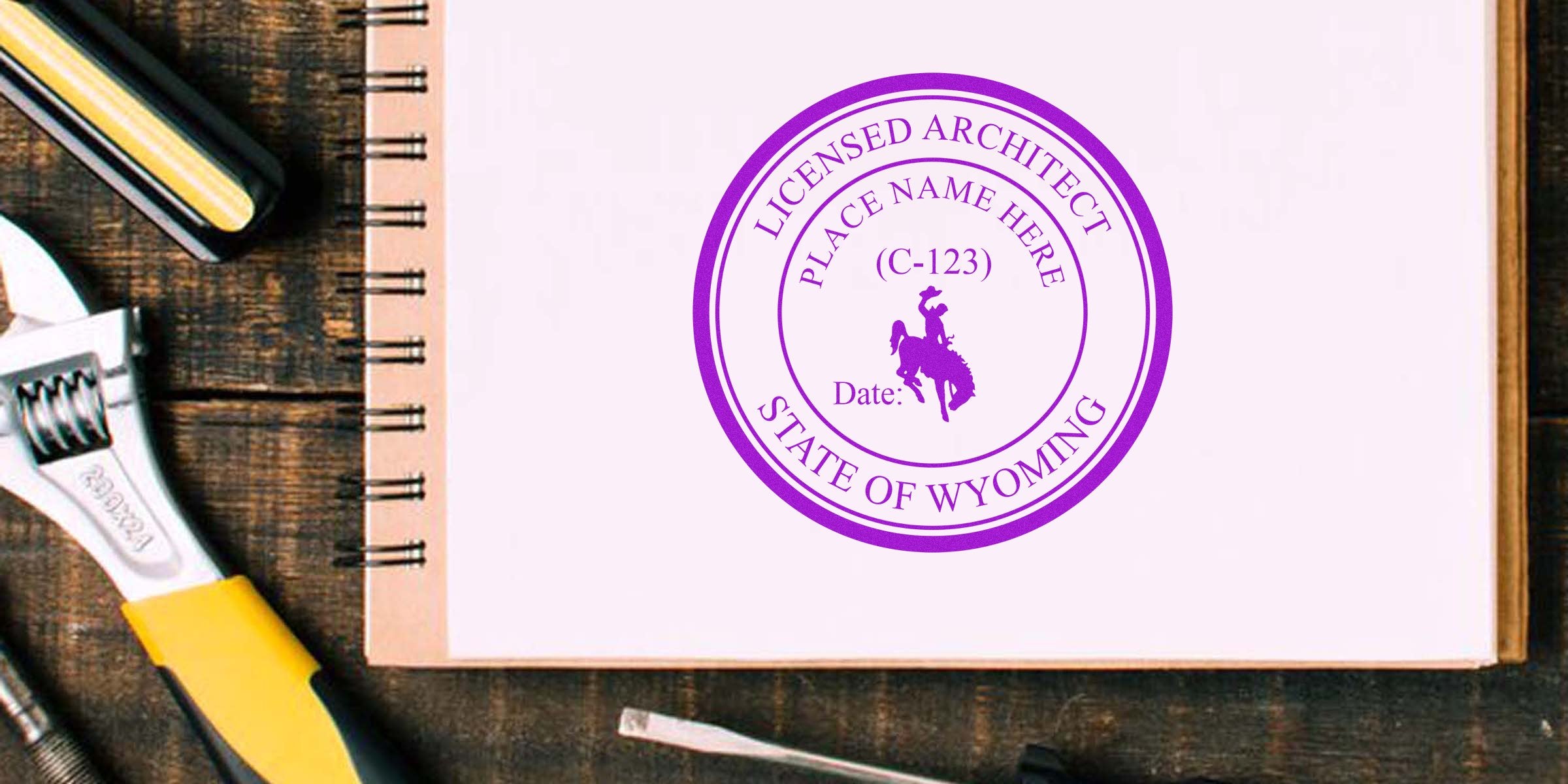 Wyoming architect stamp embossed on notebook next to wrench and screwdriver on wooden table, with professional embosser nearby.