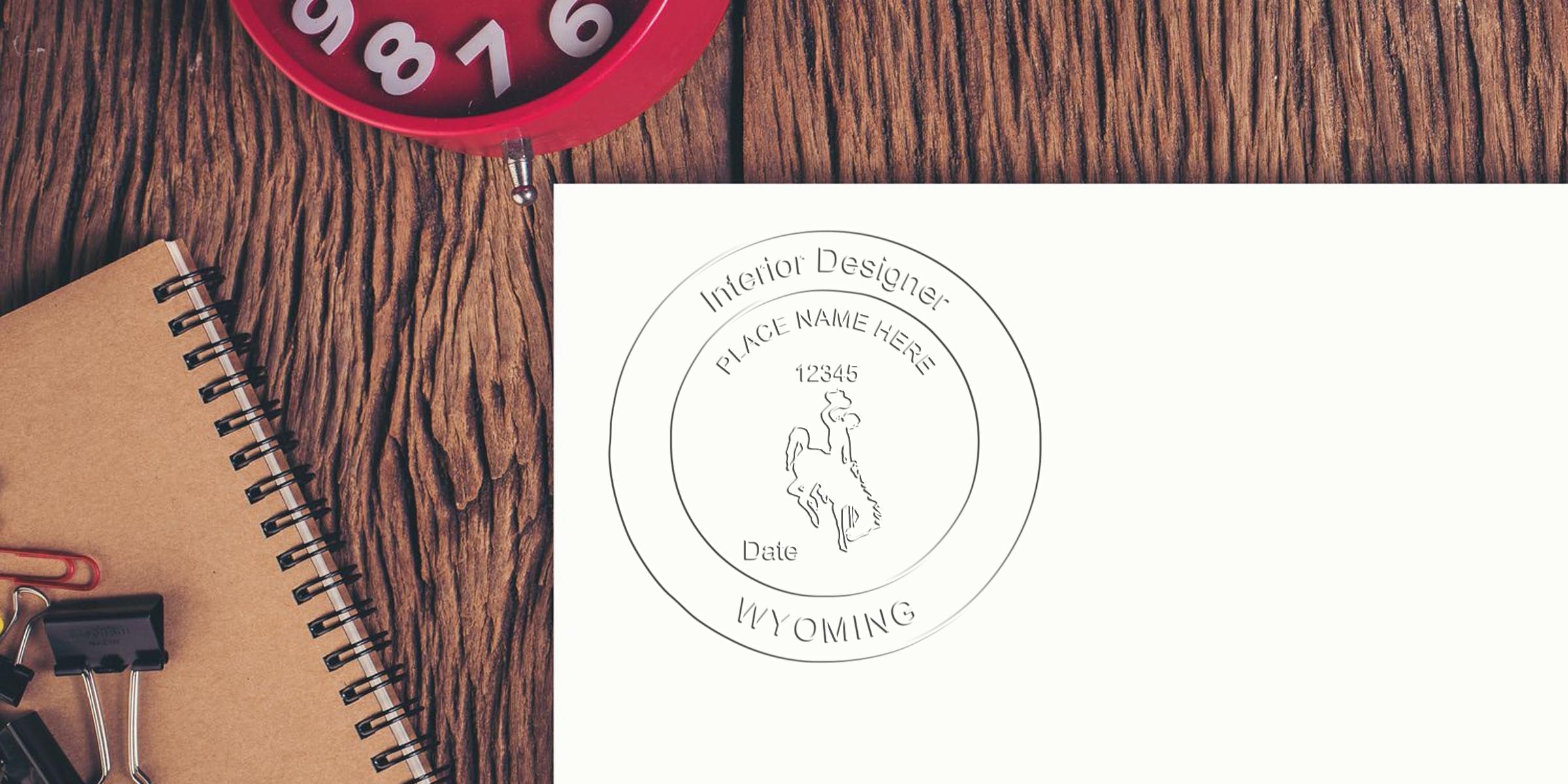 Wyoming interior design embossed stamp on white paper, placed on a wooden desk with a red clock in the background, adhering to seal design guidelines.