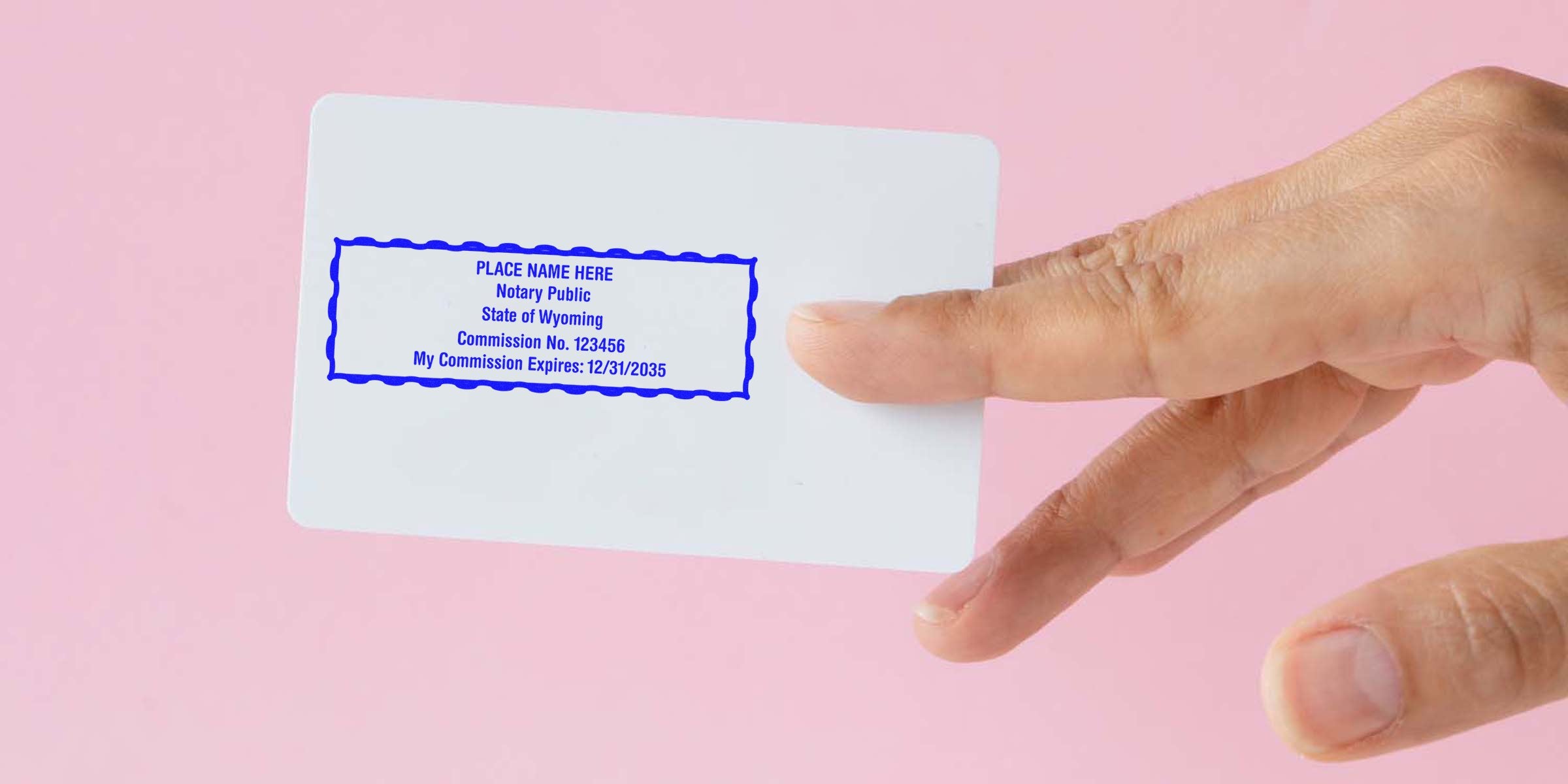 Hand holding Wyoming notary commission card with expiration date and seal against pink background, showcasing compliance with Wyoming notary public rules.