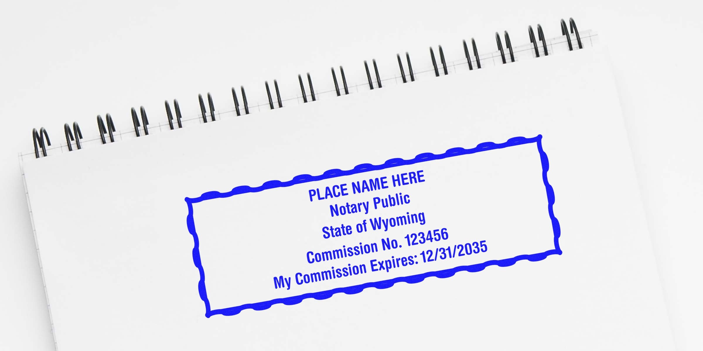 Blue Wyoming notary stamp on white spiral notebook, showing a self-inking stamp with official Wyoming notary commission and expiration date seal.