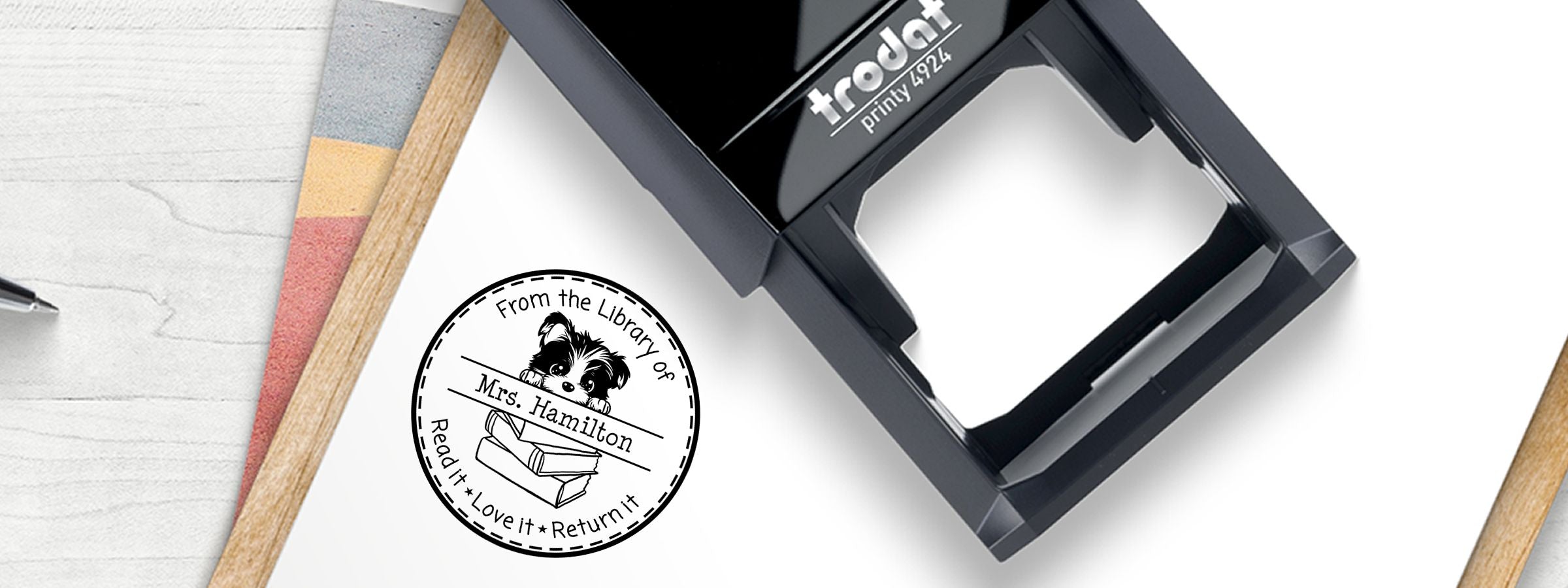 Black Trodat Printy 4924 beside a library seal; Biewer Terrier Dog Stamps and Custom Seals on a desk with notebook pages and swatches.