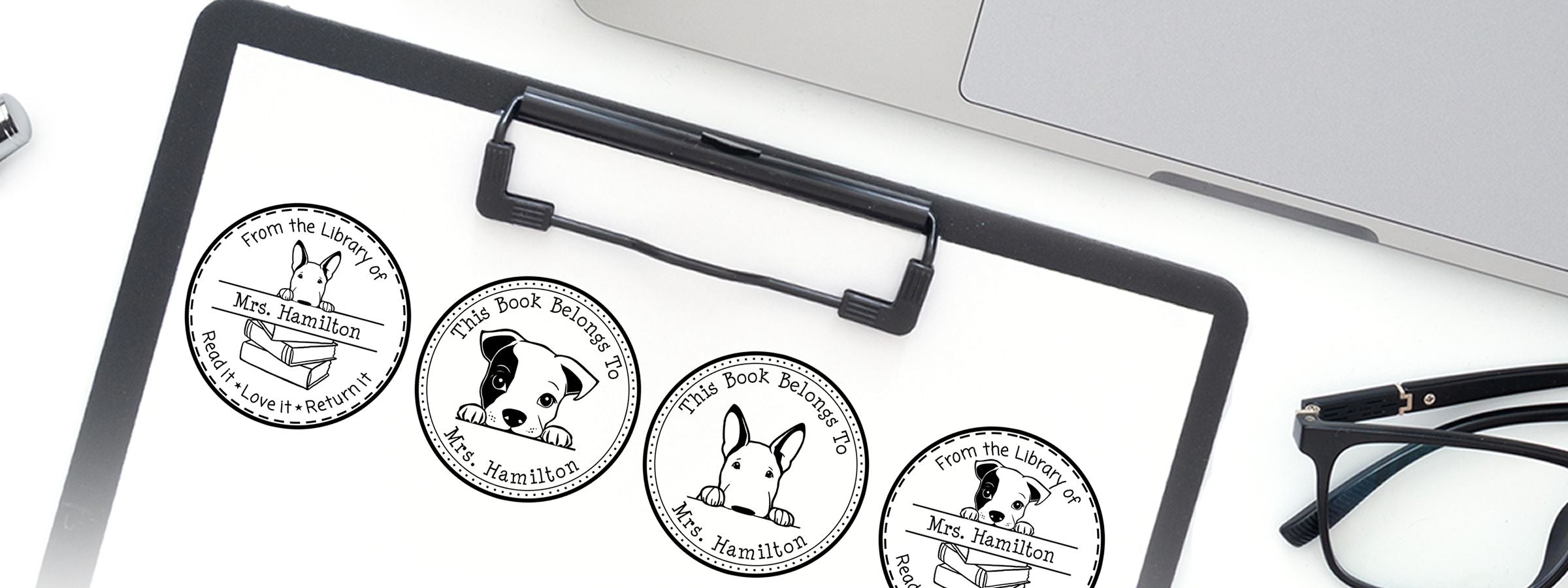Clipboard with four dog bookplate stickers for Mrs. Hamilton beside a laptop and glasses, featuring Bull Terrier Dog Stamps and Custom Seals.