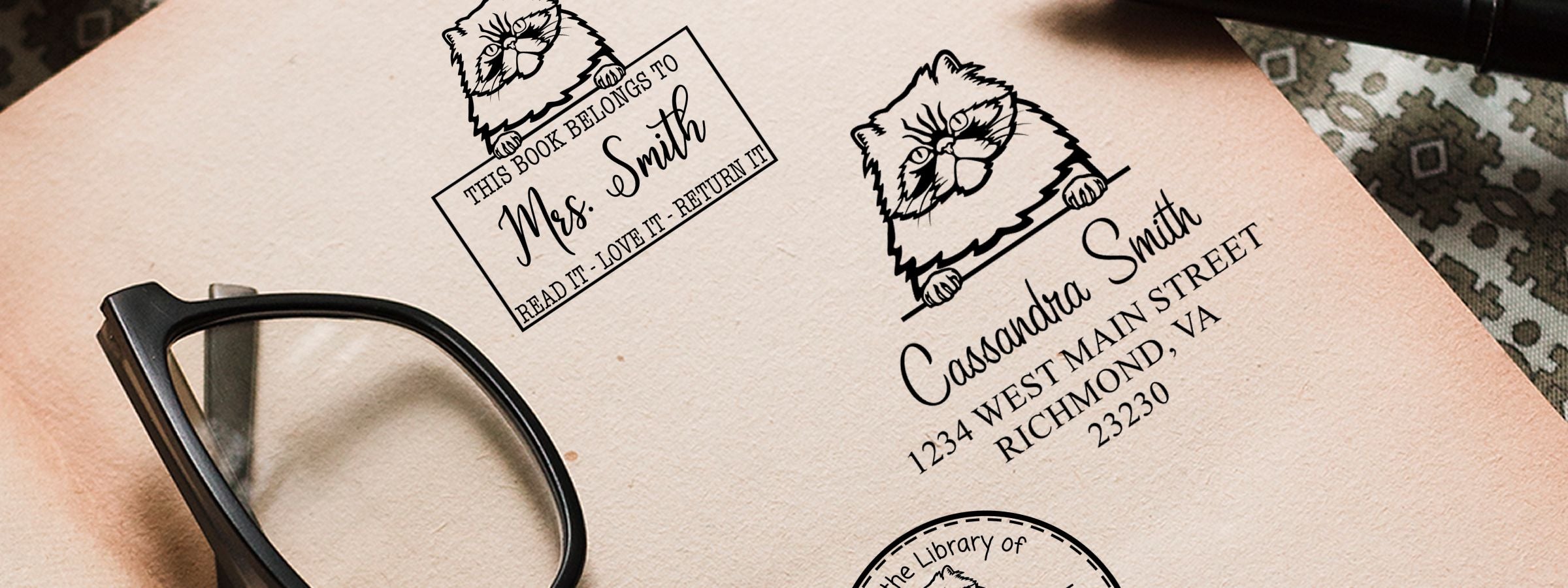 Close-up of a tote bag with cat-and-book art, personalized library label text, and black eyeglasses; Colorpoint Persian Cat Stamps and Custom Seals.