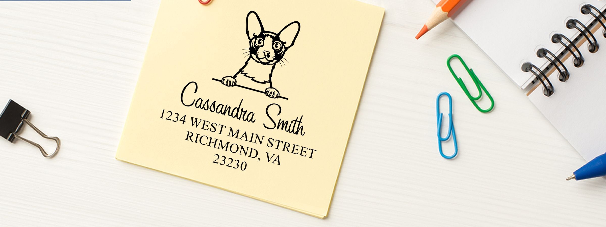 Yellow notepad with dog sketch, Cassandra Smith address, pens, clips, and Cornish Rex Cat Stamps and Custom Seals on a white desk.