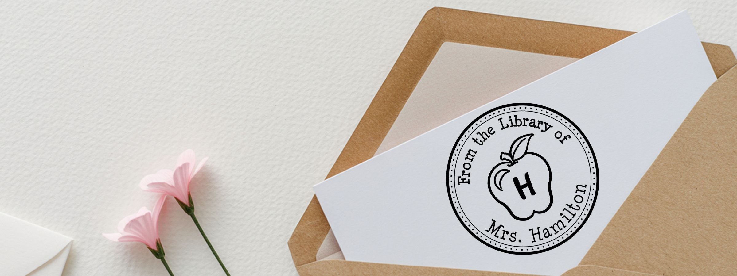 Open brown envelope with white card logo and pink flowers, showcasing Custom Designer Stamps.