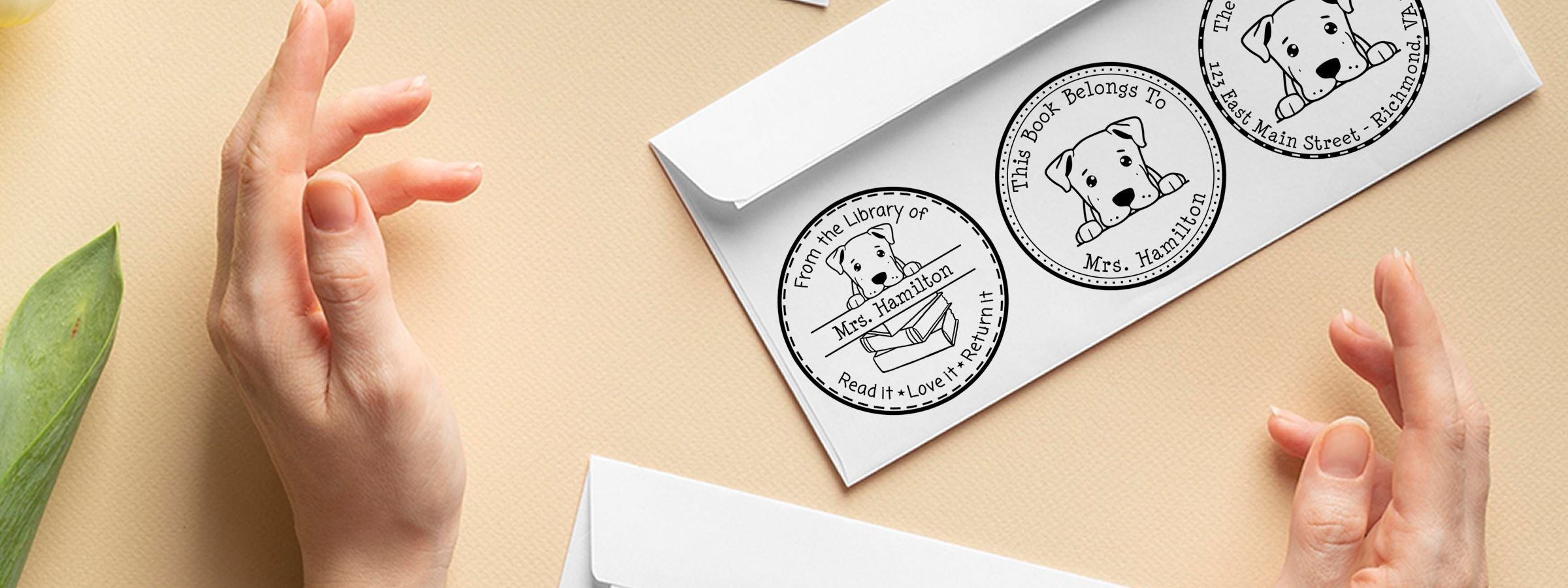 Hands frame a white envelope with Dogo Argentino Dog Stamps and Custom Seals, featuring Mrs. Hamilton bookplate stamps on a beige background.