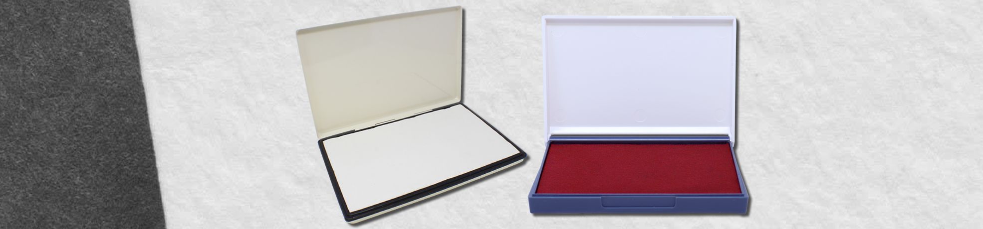 Two open presentation boxes on a light background, black with white interior and blue with red felt interior for Rubber Stamp Pads.