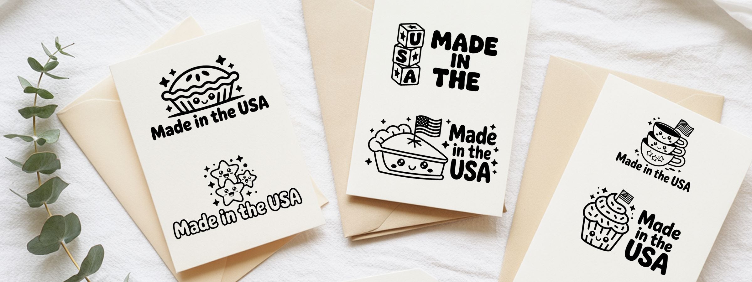 Flat lay of cream greeting cards and envelopes on white fabric with eucalyptus and Kawaii Made In USA Stamps icons like pie, stars, coffee cups, cupcake.
