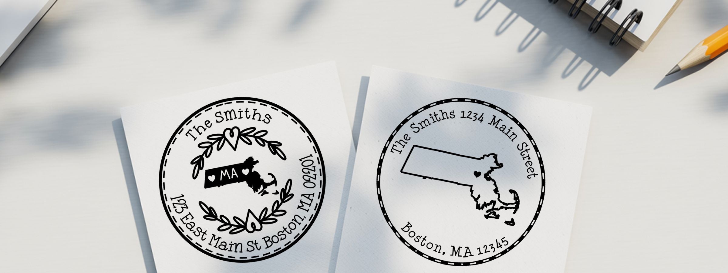 Massachusetts Designer Stamps and Seals: two black-and-white personalized round stamp proofs on a desk with pencil and notebook.