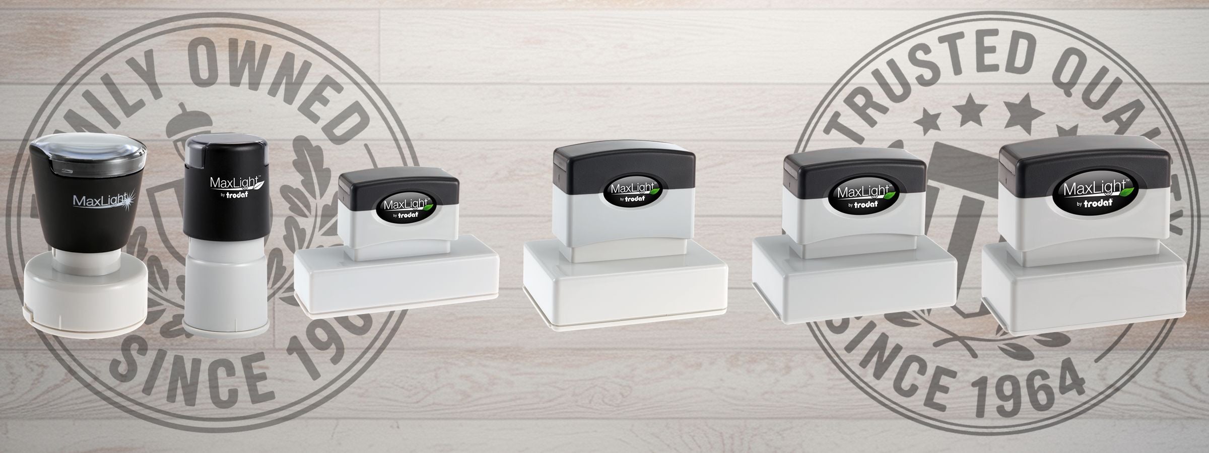Row of six MaxLight Pre-Inked Stamps by Trodat in varying sizes on light wood, with faint Family Owned and Trusted Quality Since 1964 seals.