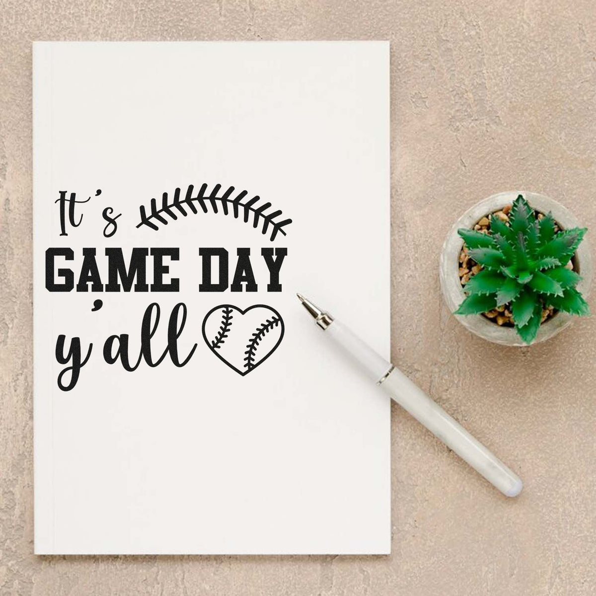 It's Game Day Y'all Slim Pre-Inked Stamp imprint stamped in black ink. A curved baseball seam and baseball heart accent "It's game day y'all."