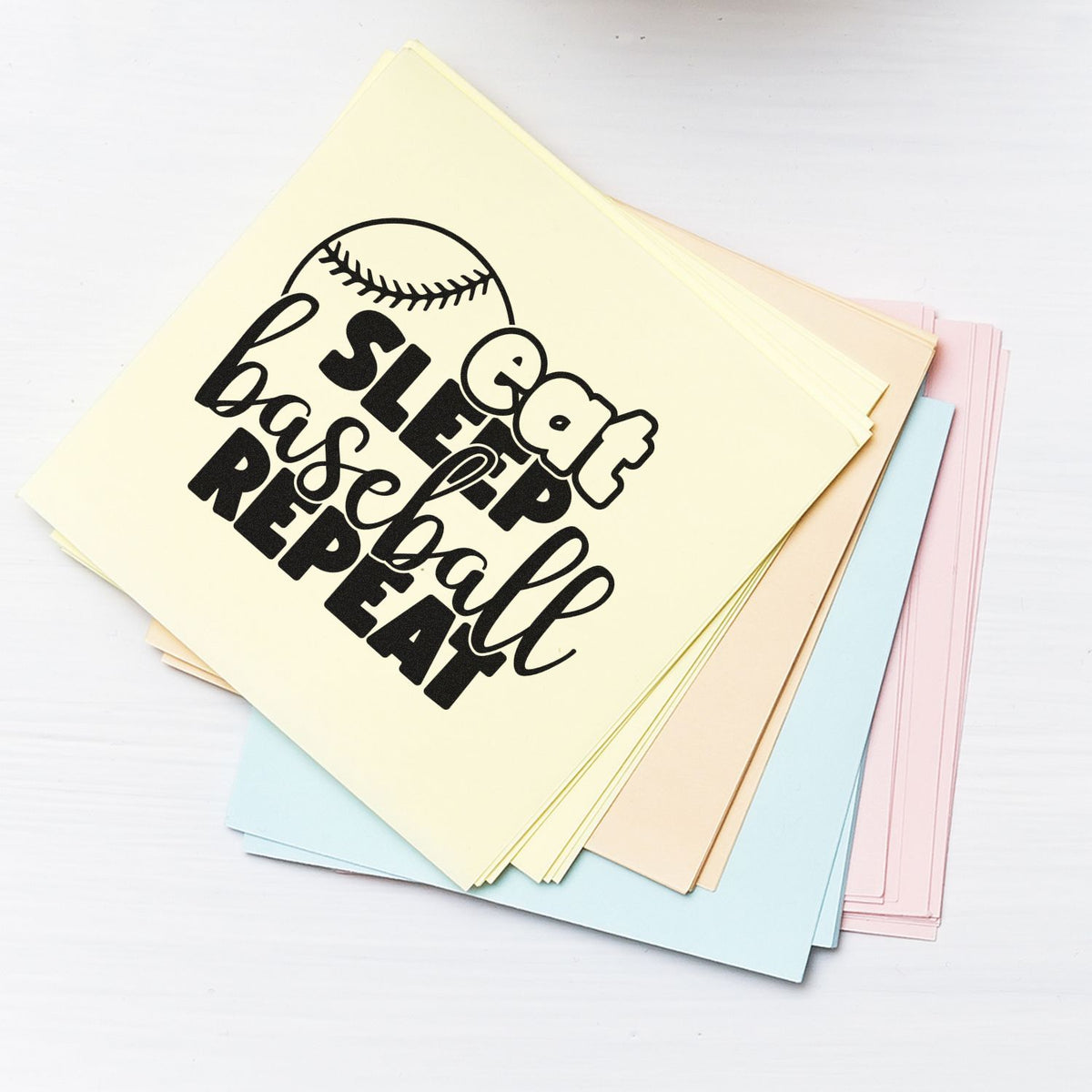 Baseball rubber stamp design with Eat Sleep Ball Repeat on pastel paper, ideal for sports-themed crafts, cards and scrapbooking.