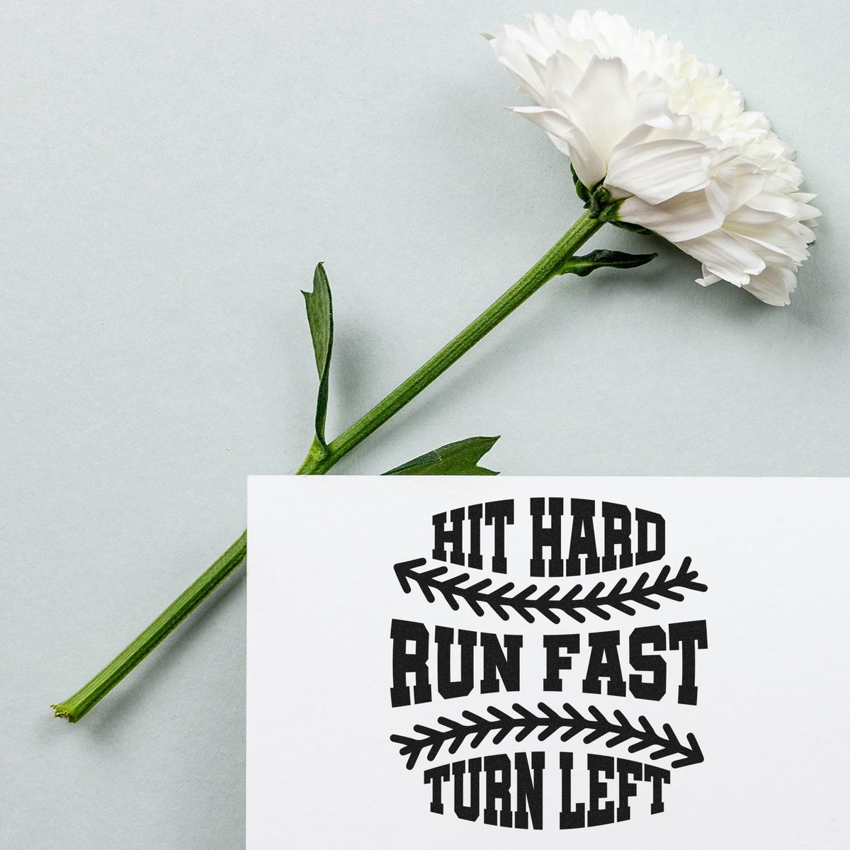 Custom rubber stamp sample with bold Hit Hard Run Fast Turn Left lettering and arrow graphics beside a white flower.