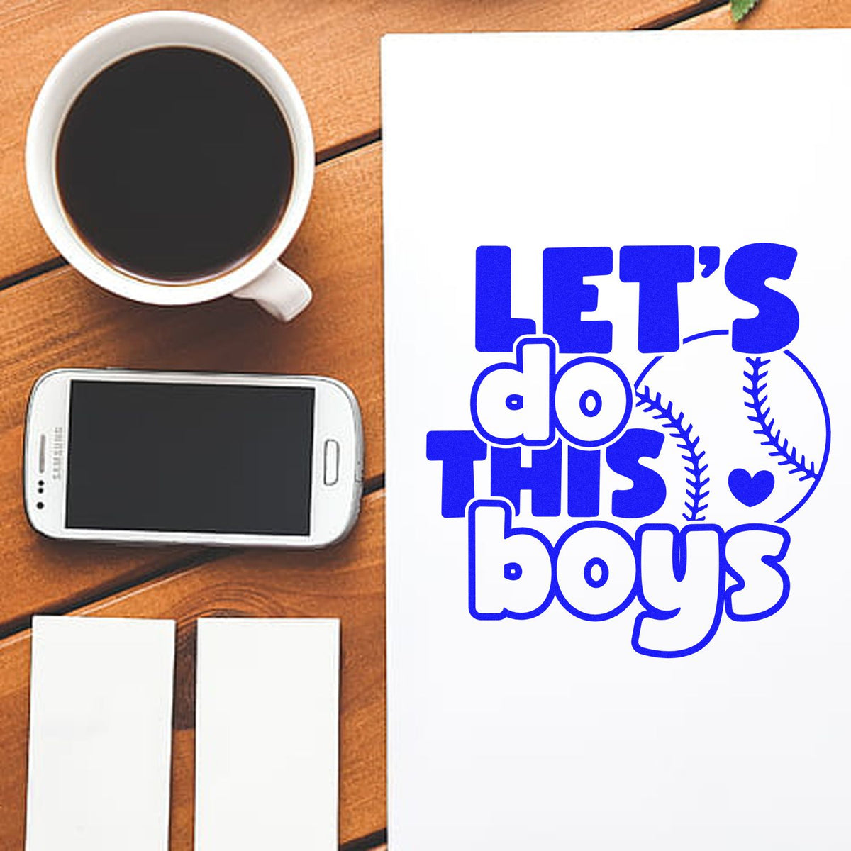 Custom baseball rubber stamp design reading Lets Do This Boys on paper, shown with coffee, phone, and blank cards.
