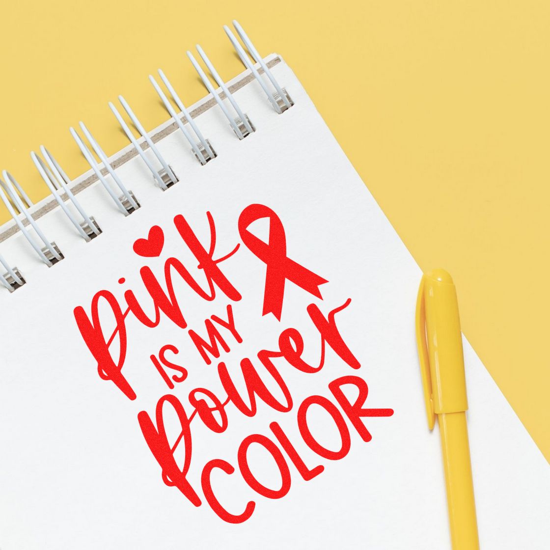 Pink is My Power Color breast cancer awareness rubber stamp on a notebook with red ribbon and yellow pen.
