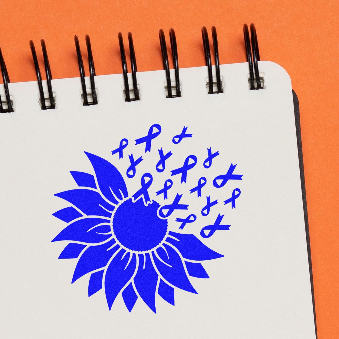 Blue awareness ribbon sunflower rubber stamp on notebook, symbolizing support for cancer awareness and advocacy.