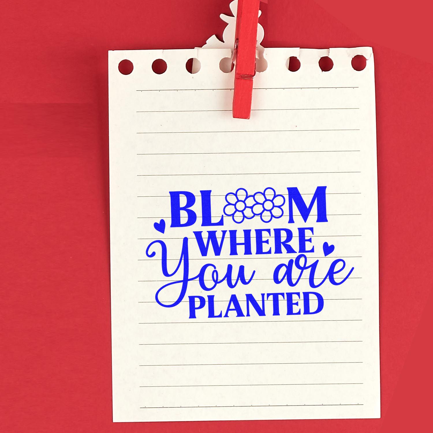Blue rubber stamp design reading Bloom Where You Are Planted with flower and heart accents on lined note paper.
