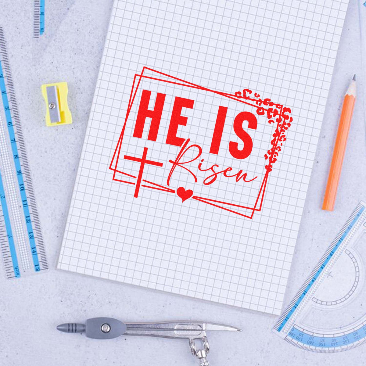 He Is Risen rubber stamp design for Easter crafts, shown in red on graph paper with school supplies.