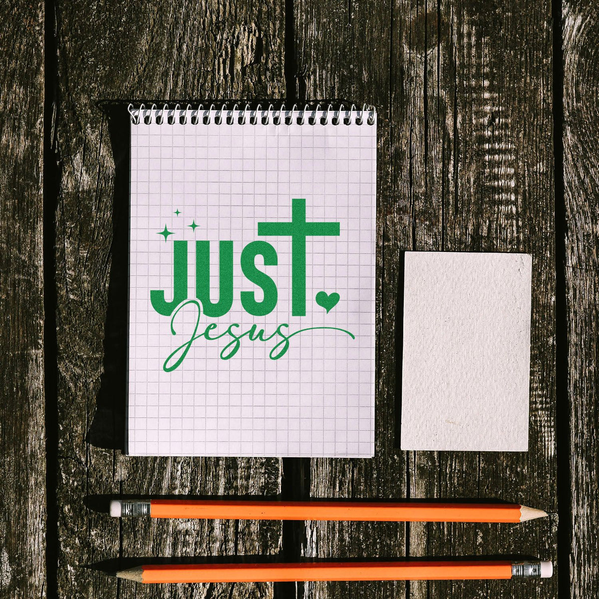 Christian custom rubber stamp design reading Just Jesus in green on a grid notebook, with sample block and pencils.