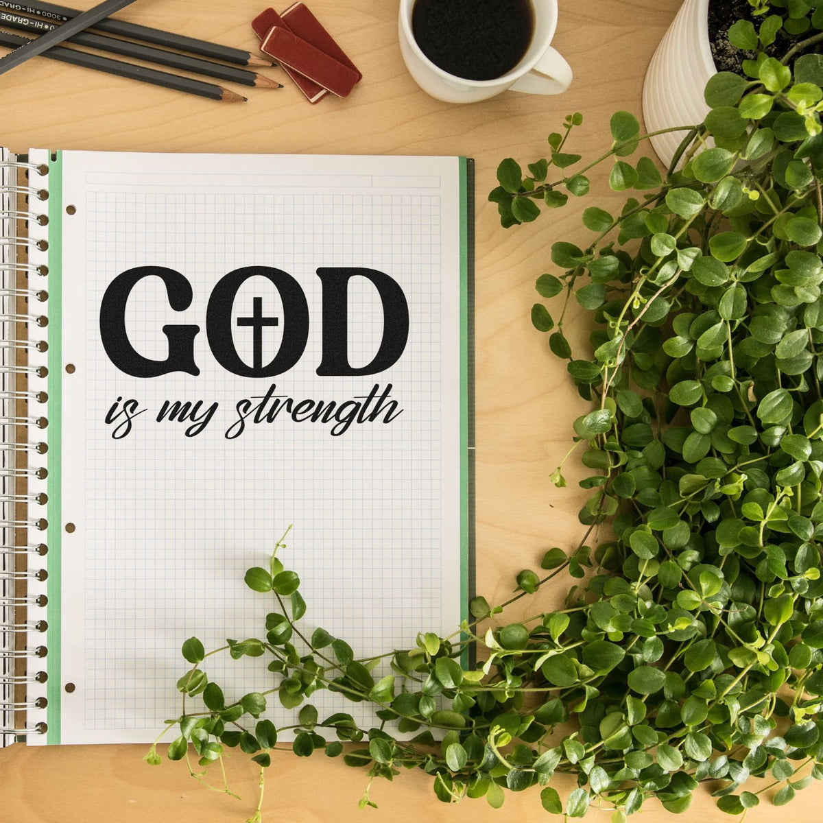 Christian rubber stamp reading God is my strength in a notebook, styled on a desk with coffee, pencils, and greenery.